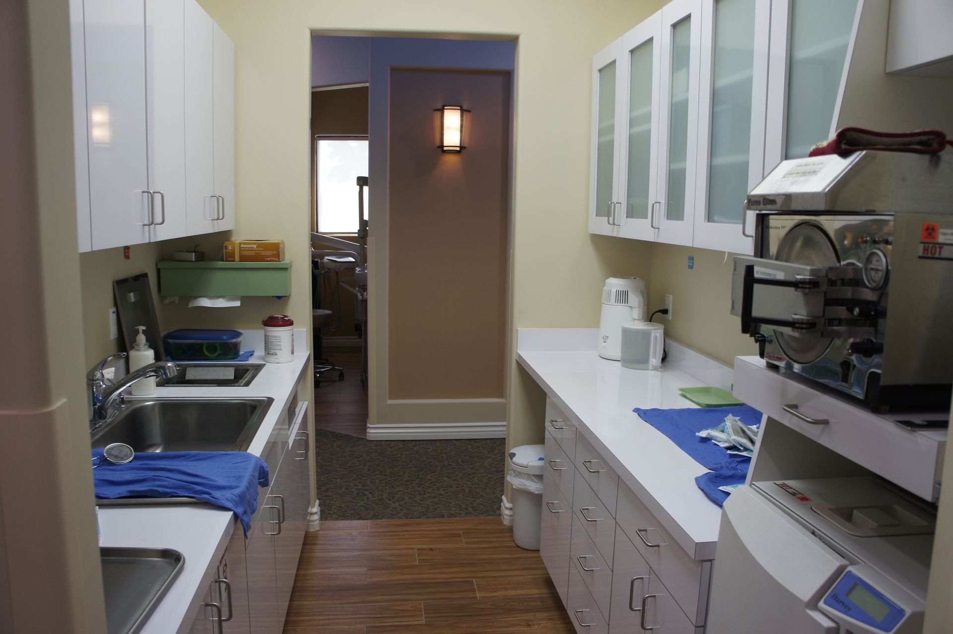 Dental office sterilization room with white cabinets, stainless steel sink, and autoclave.
