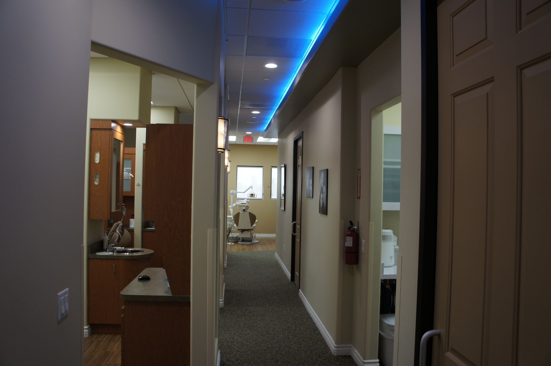 Long hallway in a dentist's office; blue overhead lighting, doors on the right, exam room at the end.