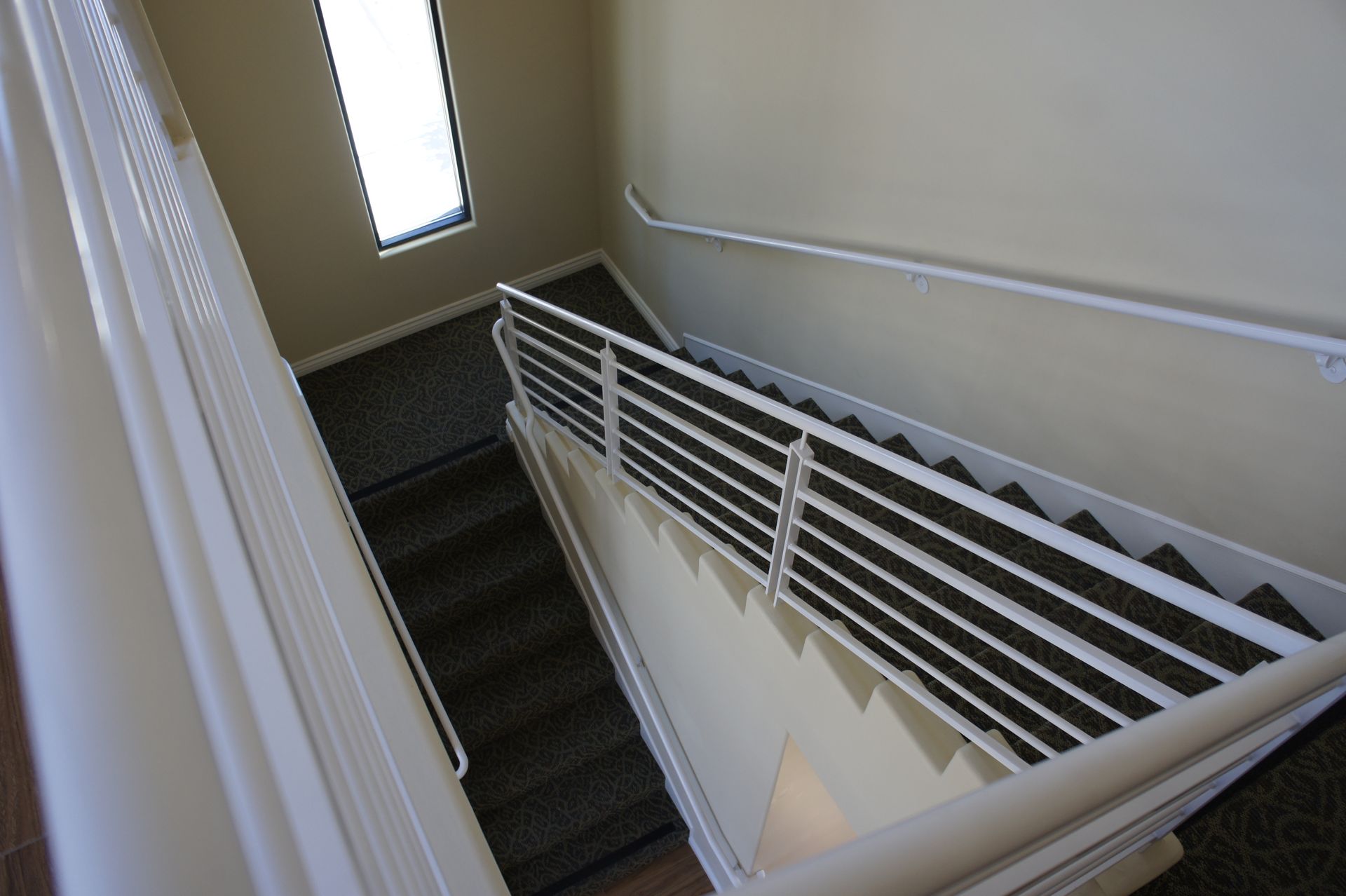 Staircase descending, with white railings and carpeted steps; a window at the top.