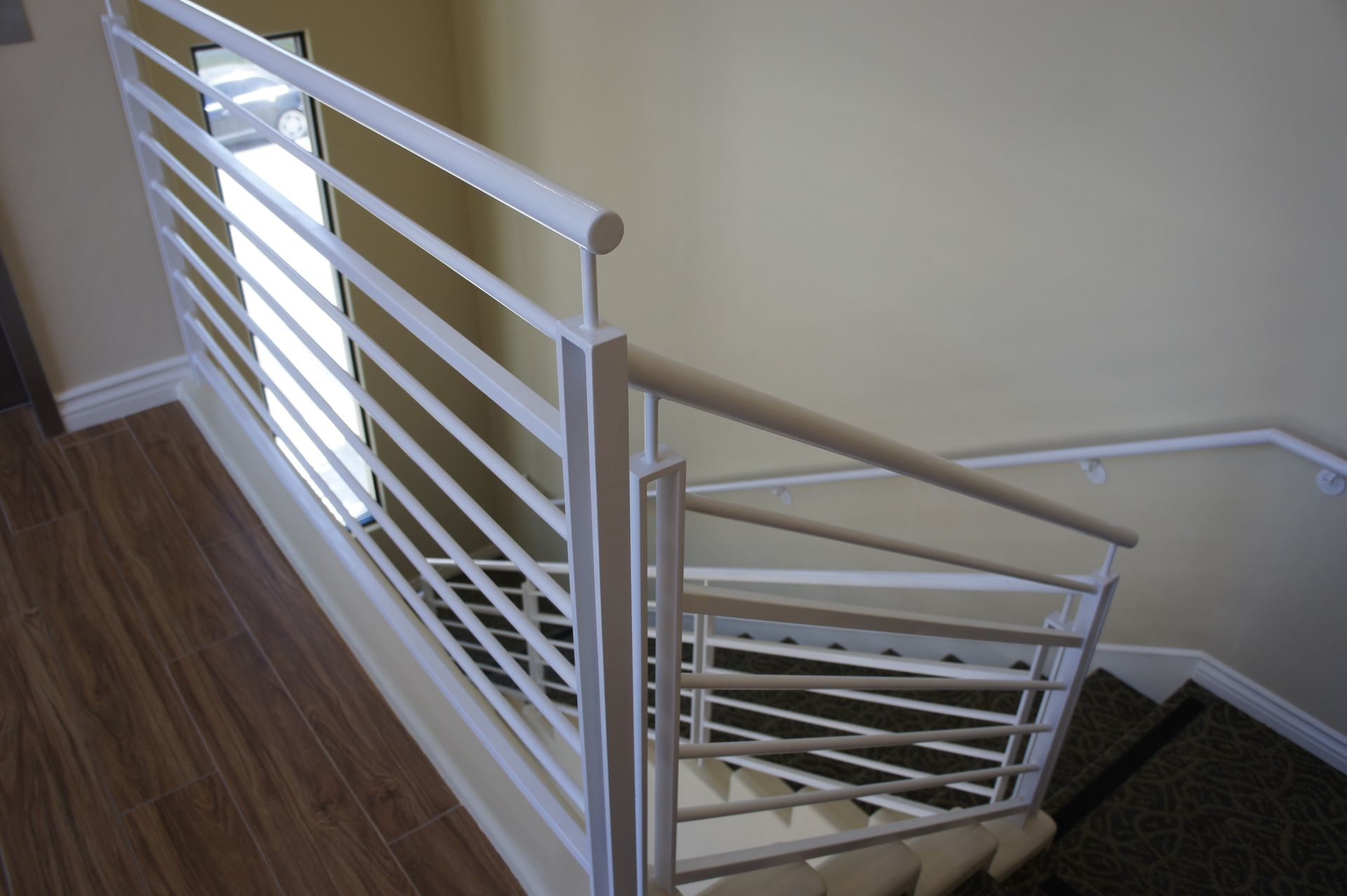 White metal railing next to a staircase with wooden flooring and beige walls.