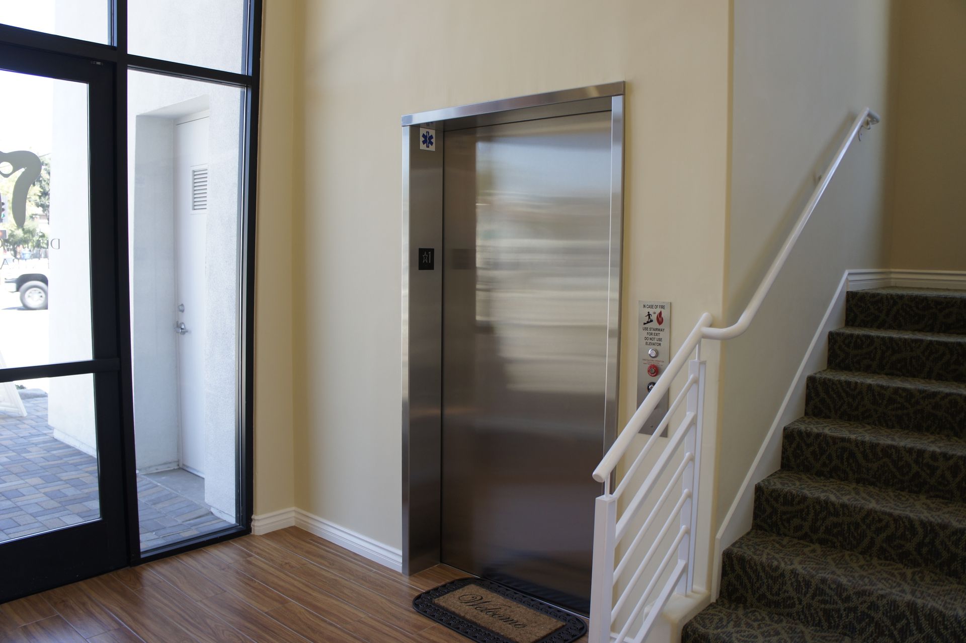 Elevator with call buttons next to staircase and open door in a building.