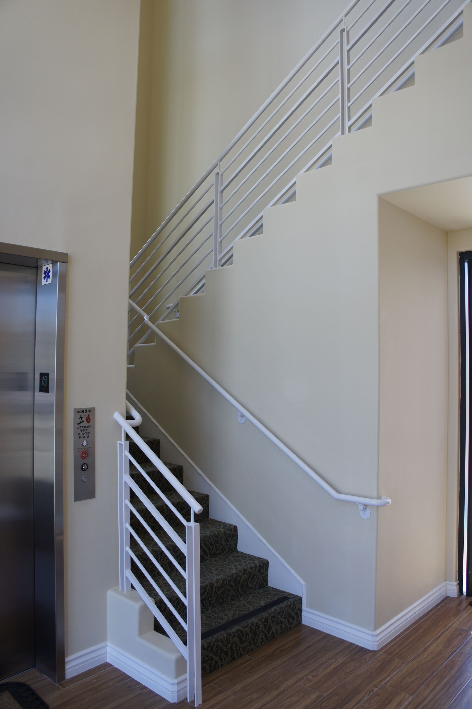 Staircase and elevator in a building's interior. White railings and tan walls.