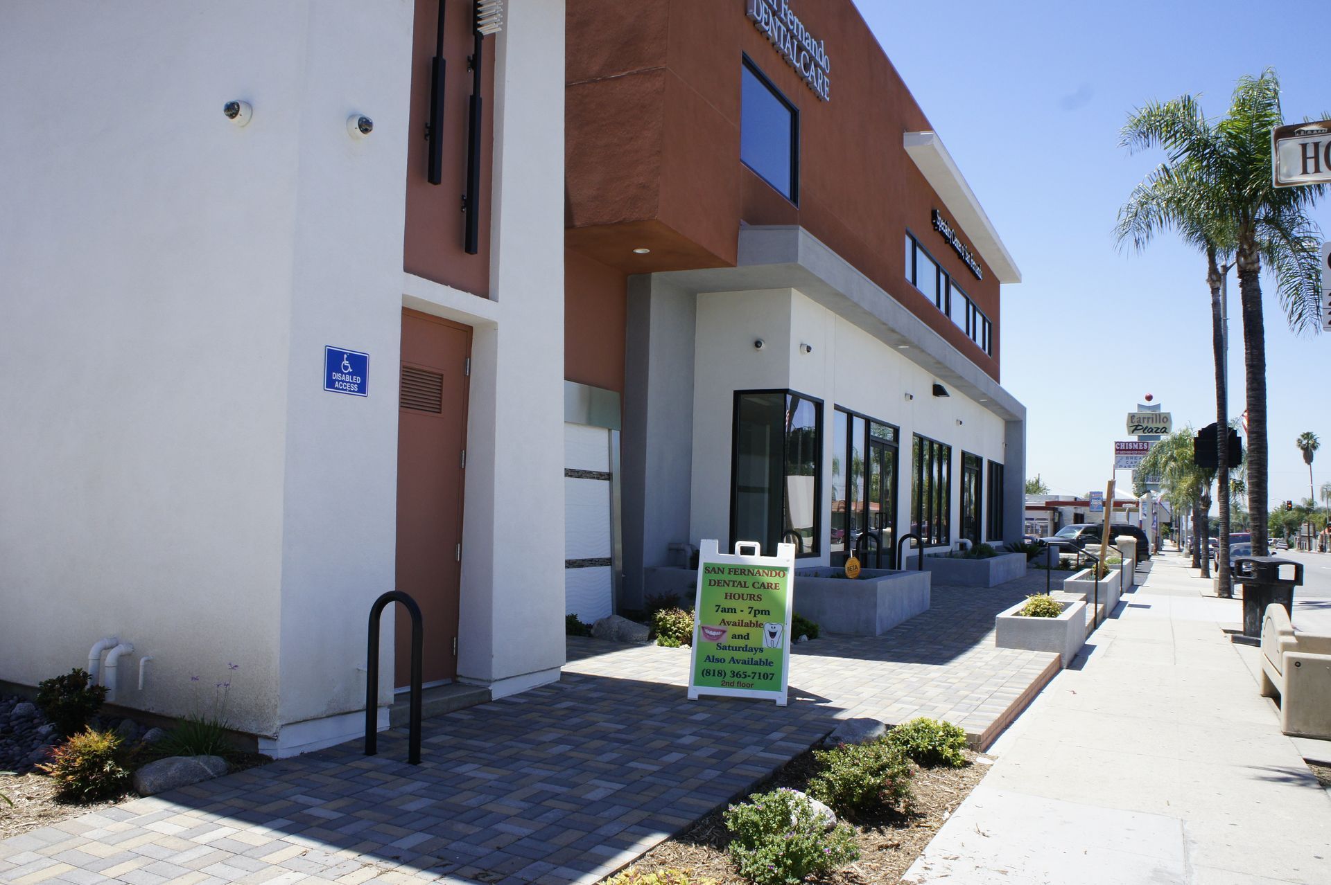 Exterior view of a modern building with a sidewalk, accessible entrance, and palm trees.