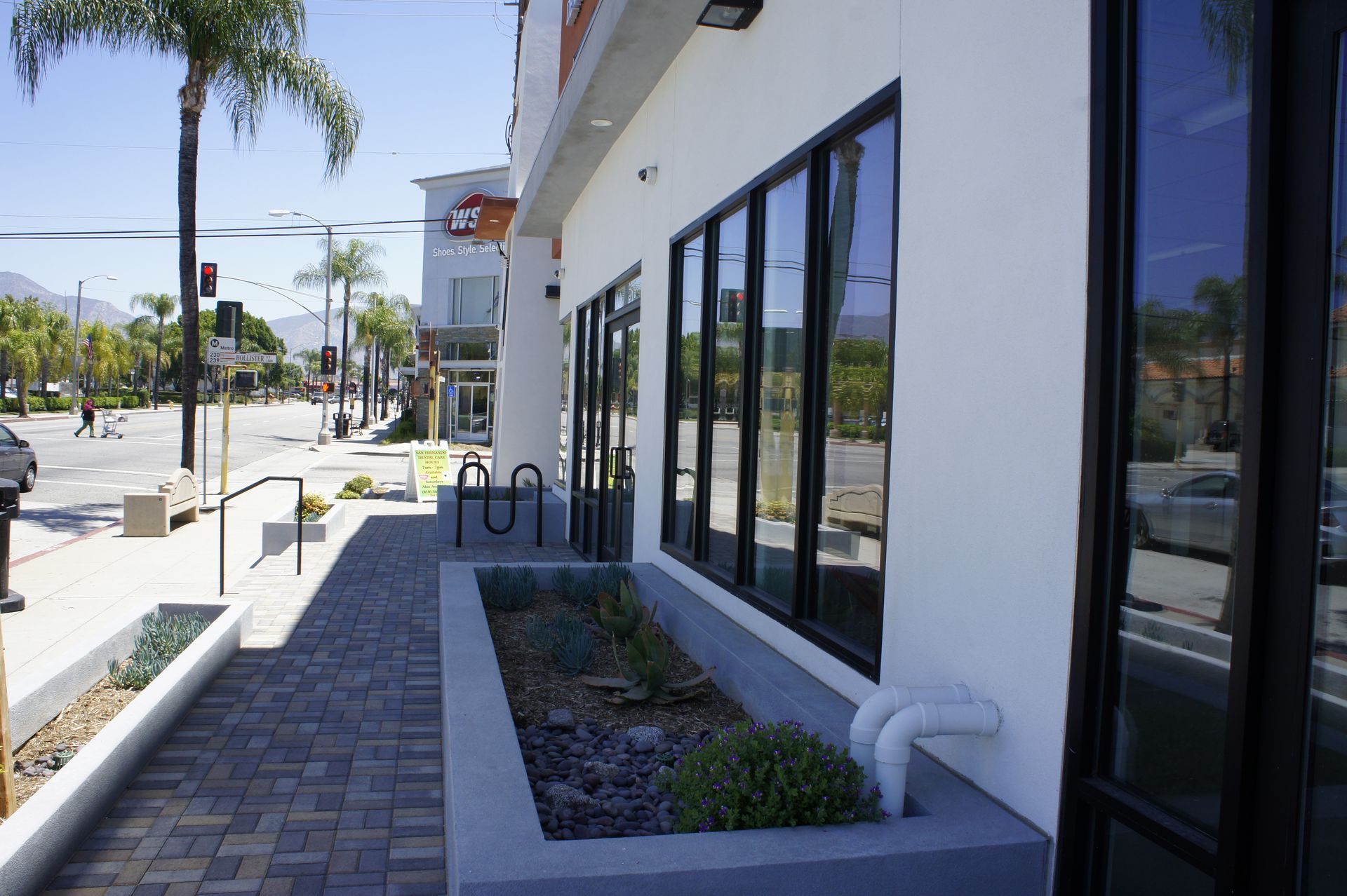 Exterior of building with large windows, small garden, brick walkway, and street in background.