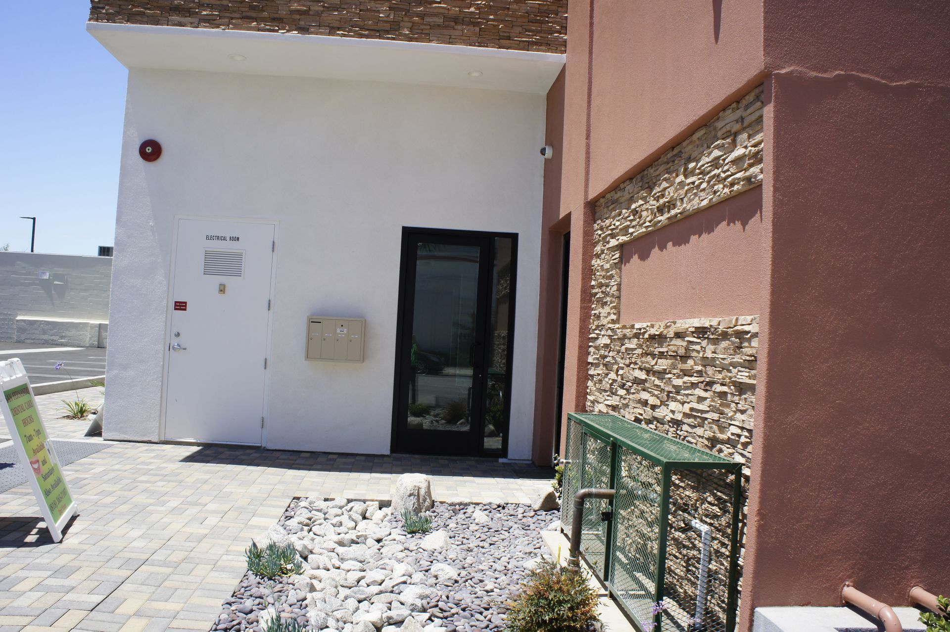 Exterior of a building with a white wall, dark door, and brick and stone accents. A sign is in the foreground.