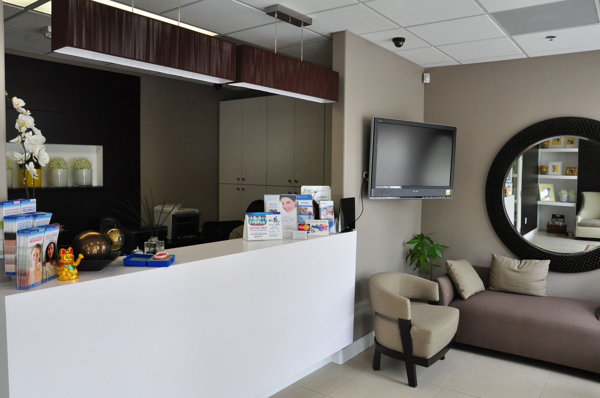 Reception area with white counter, TV, mirror, seating, and brochures.