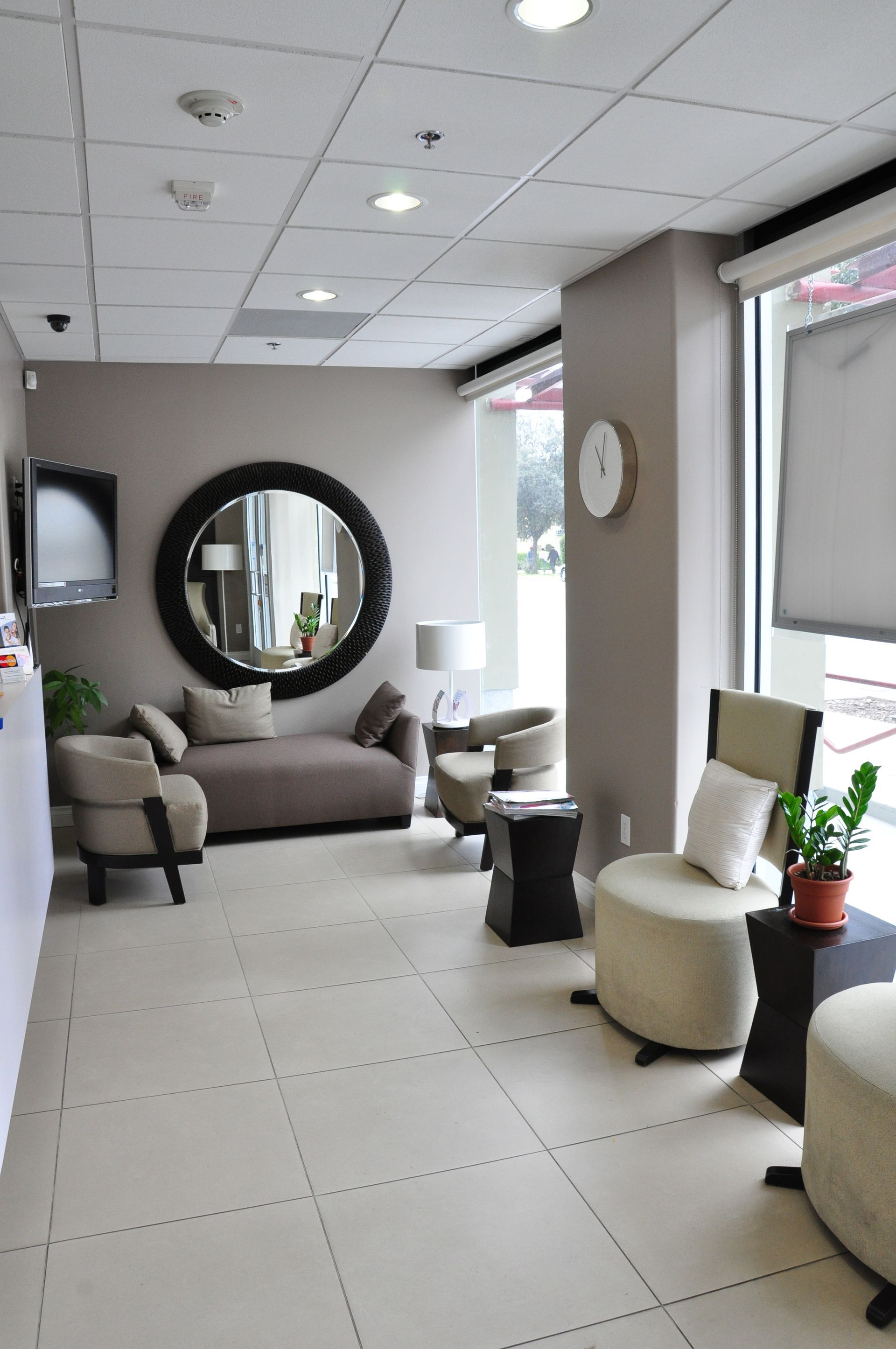 Waiting room with neutral tones. Brown sofa, beige chairs, round mirror.