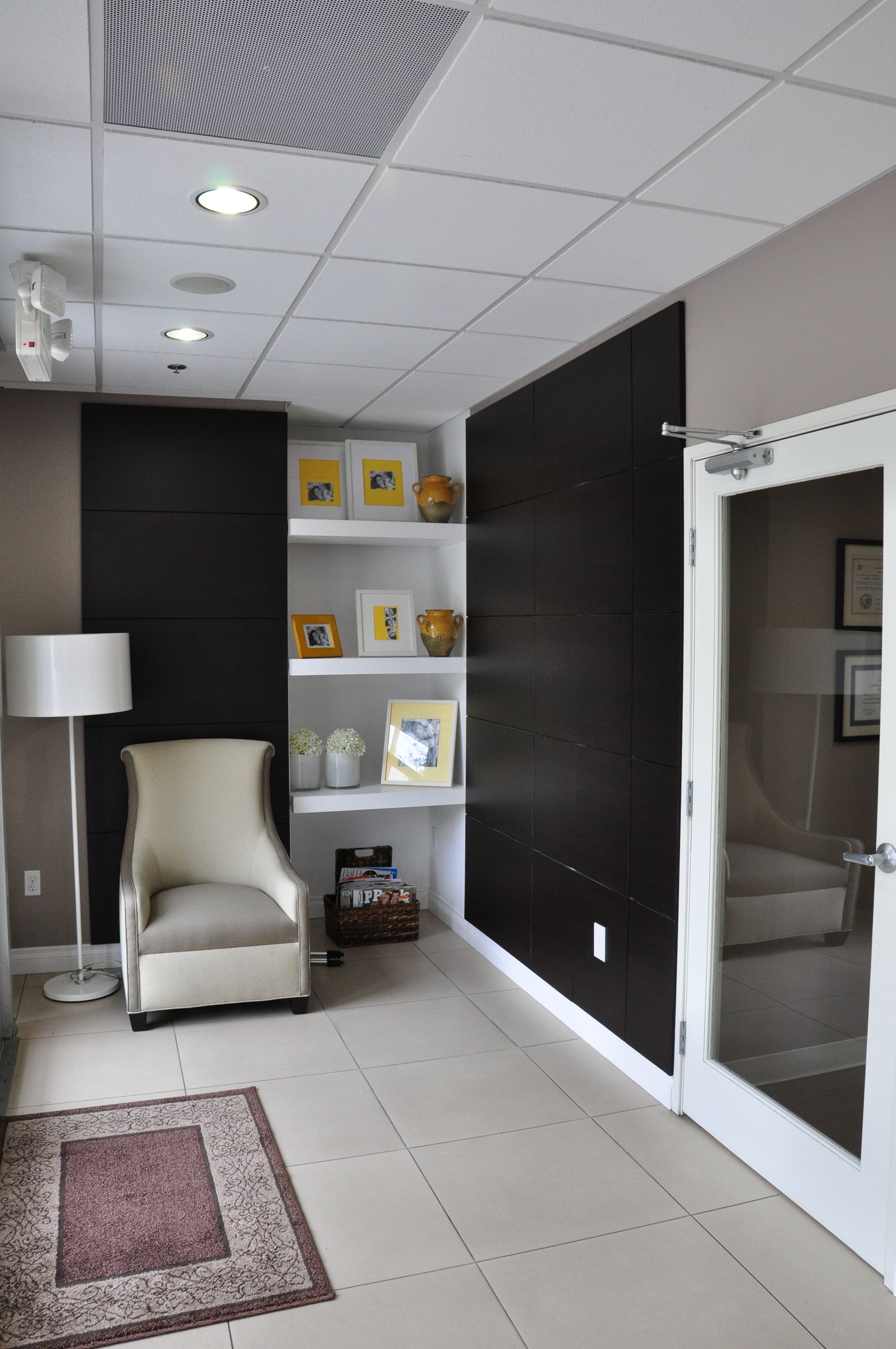 Beige chair, bookshelves, and dark accent walls in an office lobby. Light and airy with tiled flooring.