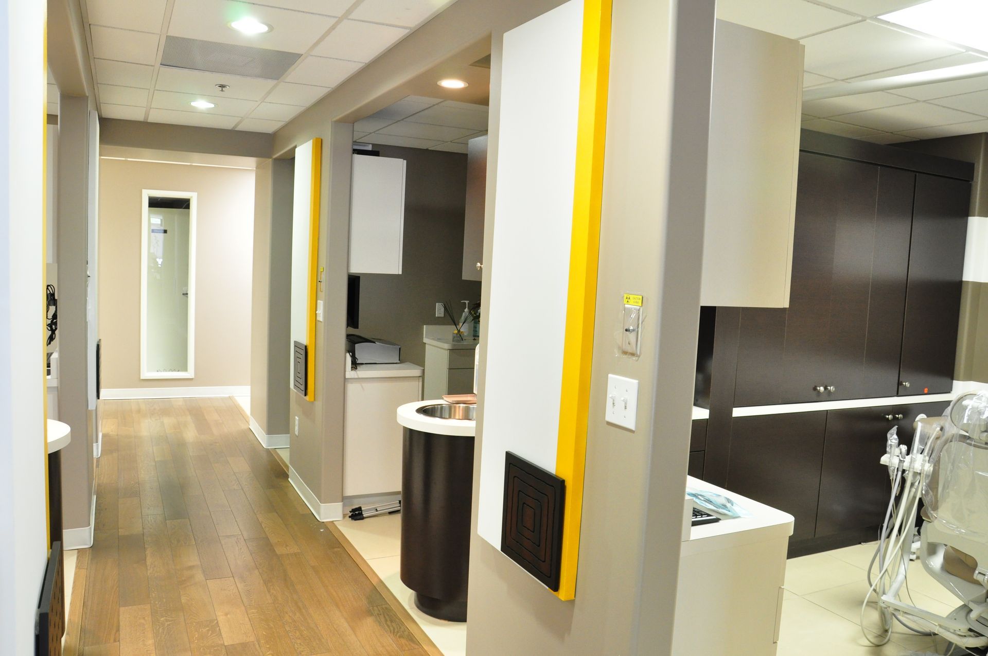 Hallway in a dental clinic with brown wooden floors, gray walls, and dental equipment.
