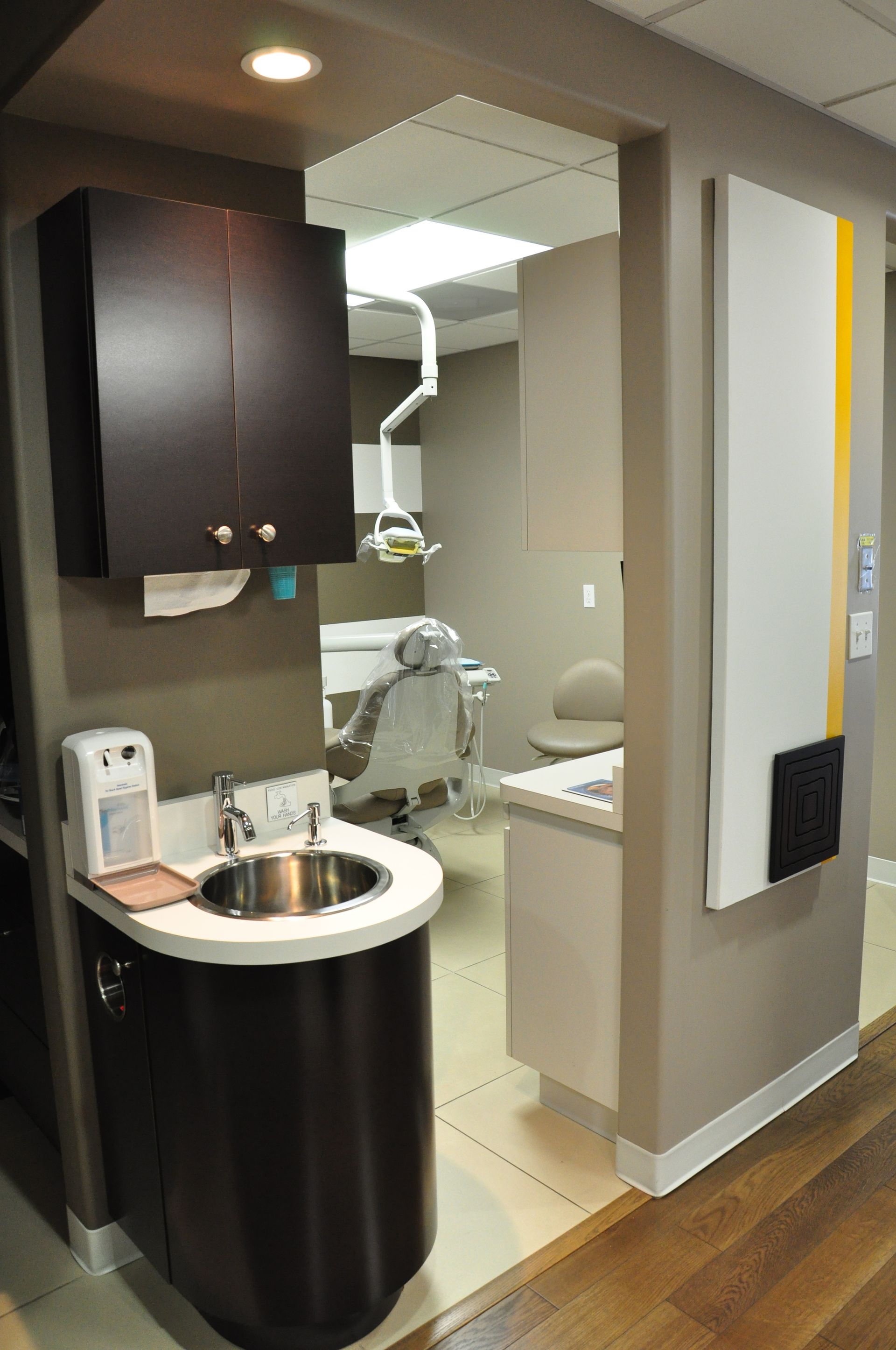 Dental office entrance, with sink, cabinets, and a view into an exam room with dental chair.