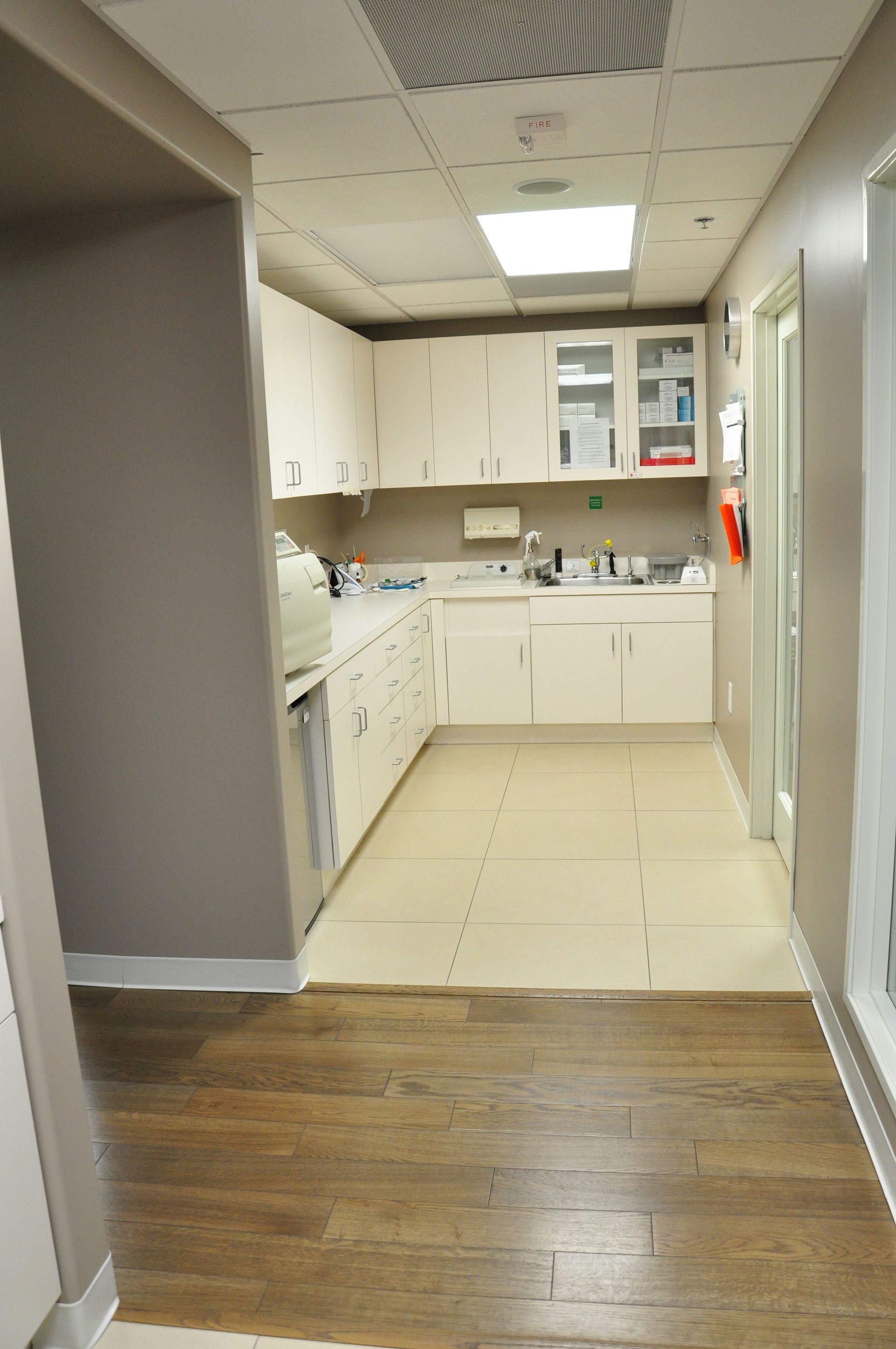 Narrow medical office hallway with white cabinets, beige countertops, and wood-look flooring.