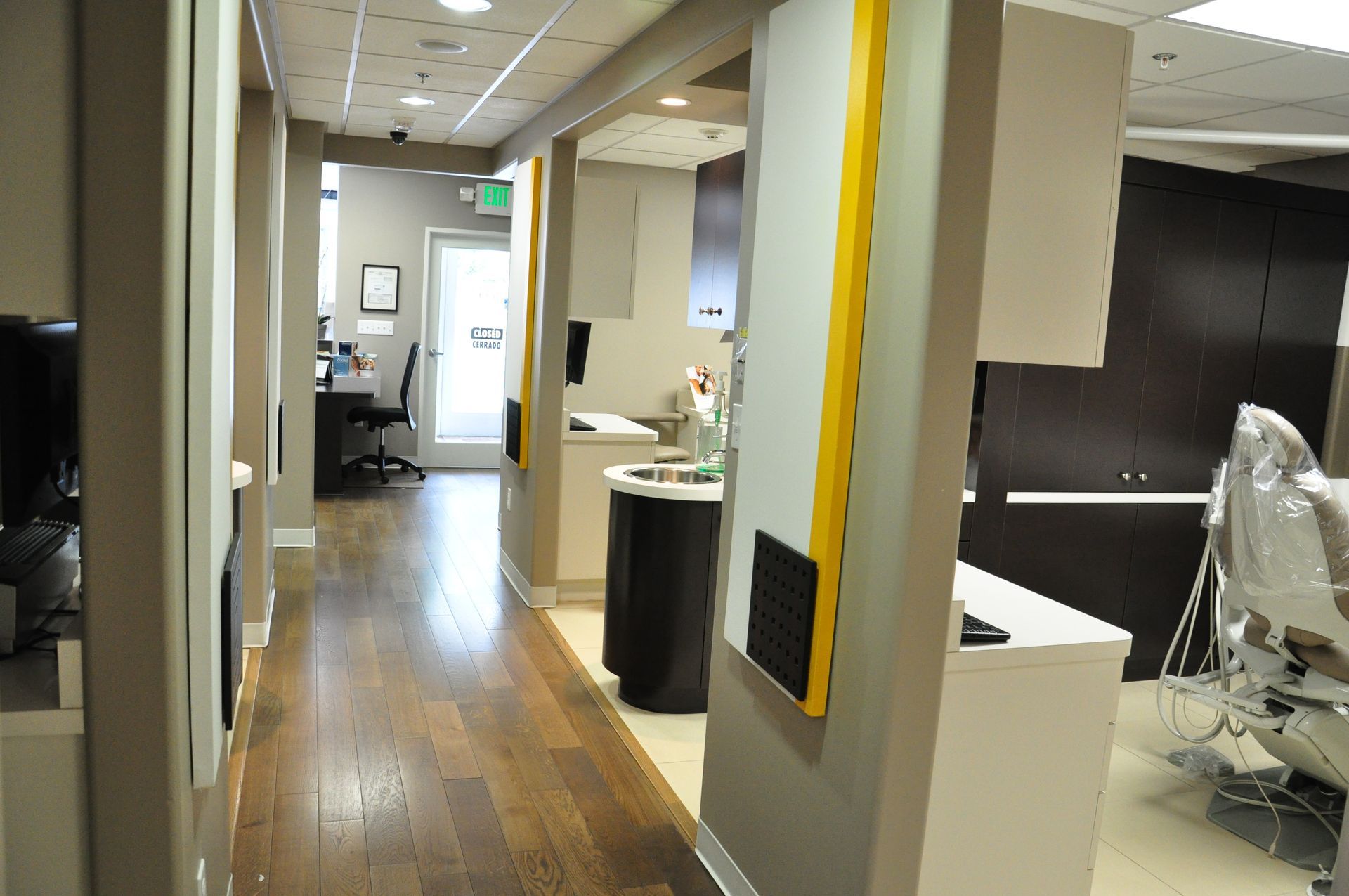 Hallway in a dental office with examination rooms, wood floors, and white and yellow accents.