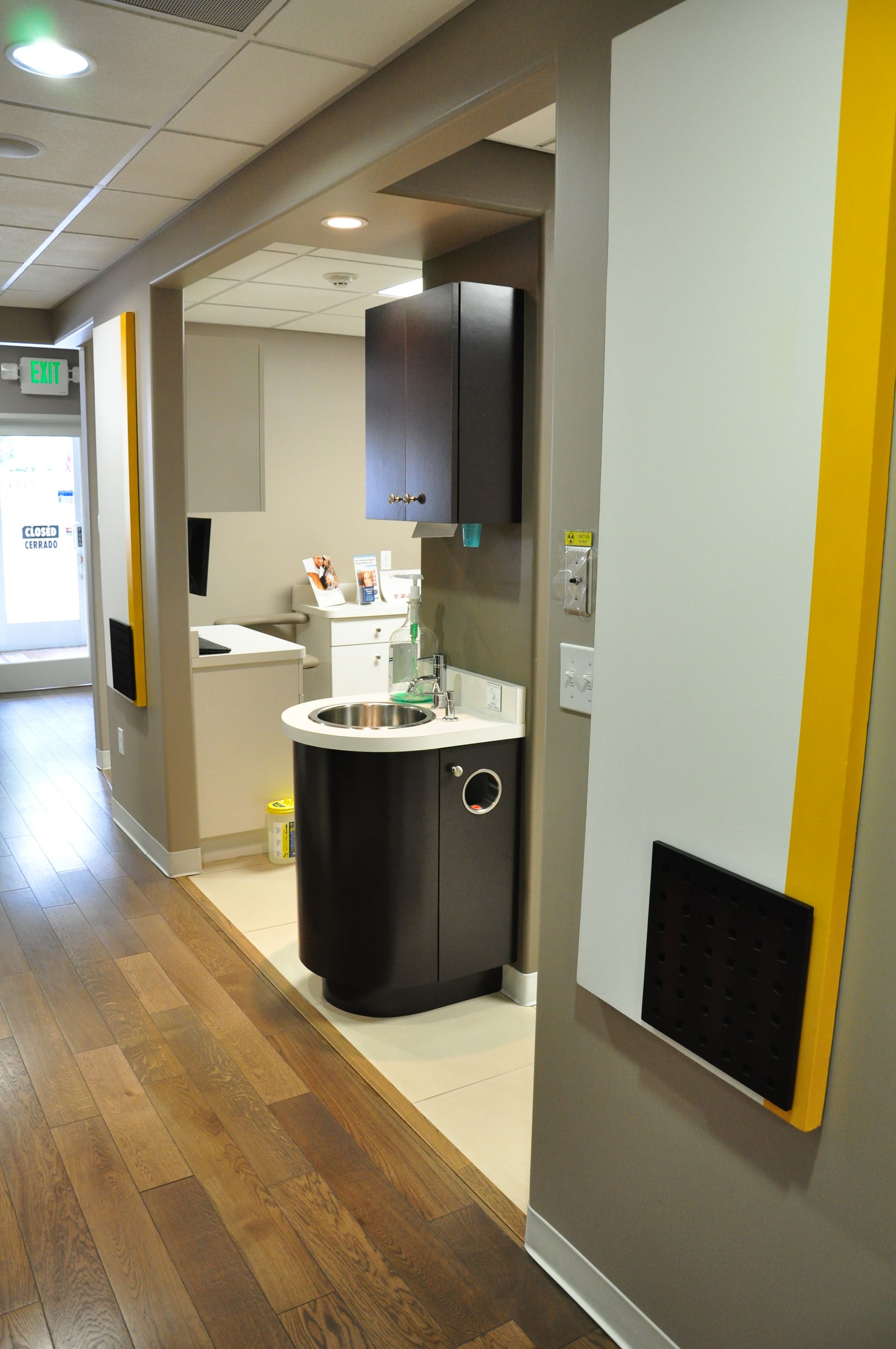 Hallway in a dental office with sink, cabinetry, and wooden floors. Yellow and white wall panels.
