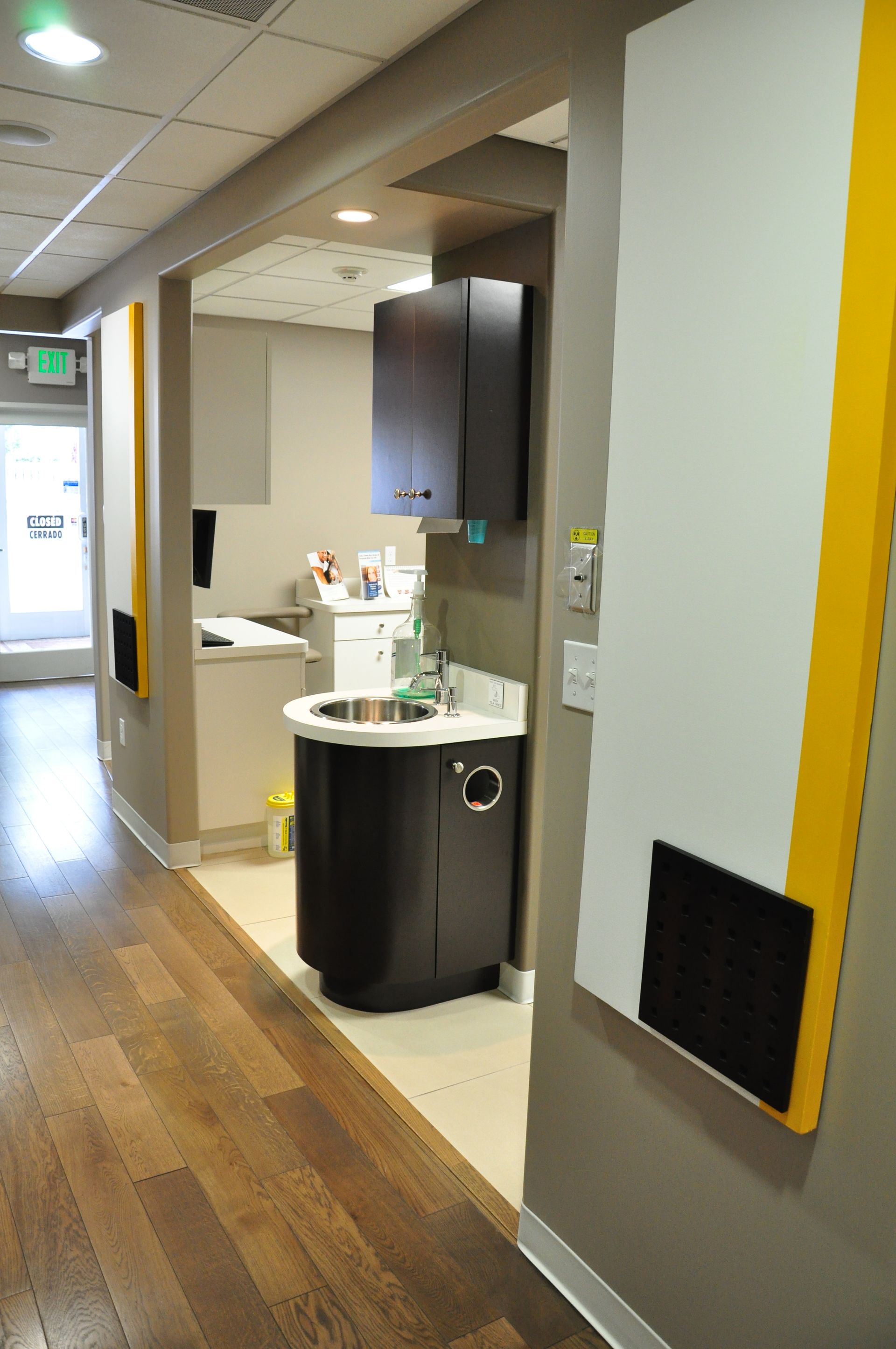 Hallway in a dental office with examination rooms and sinks. Features neutral tones and wood flooring.