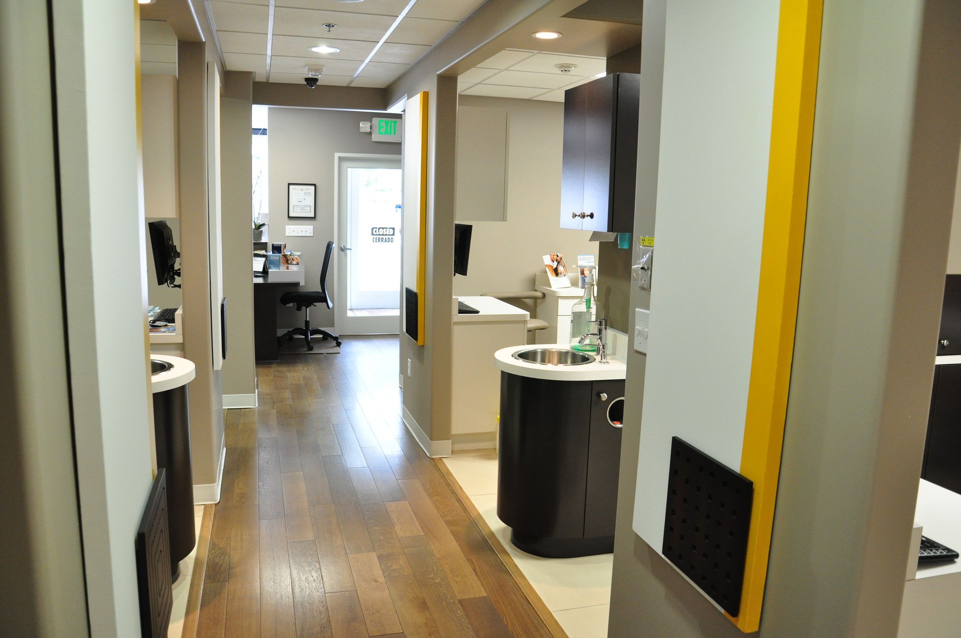 Hallway in a dental office, featuring patient rooms, sinks, wooden floor, and a doorway to the reception area.