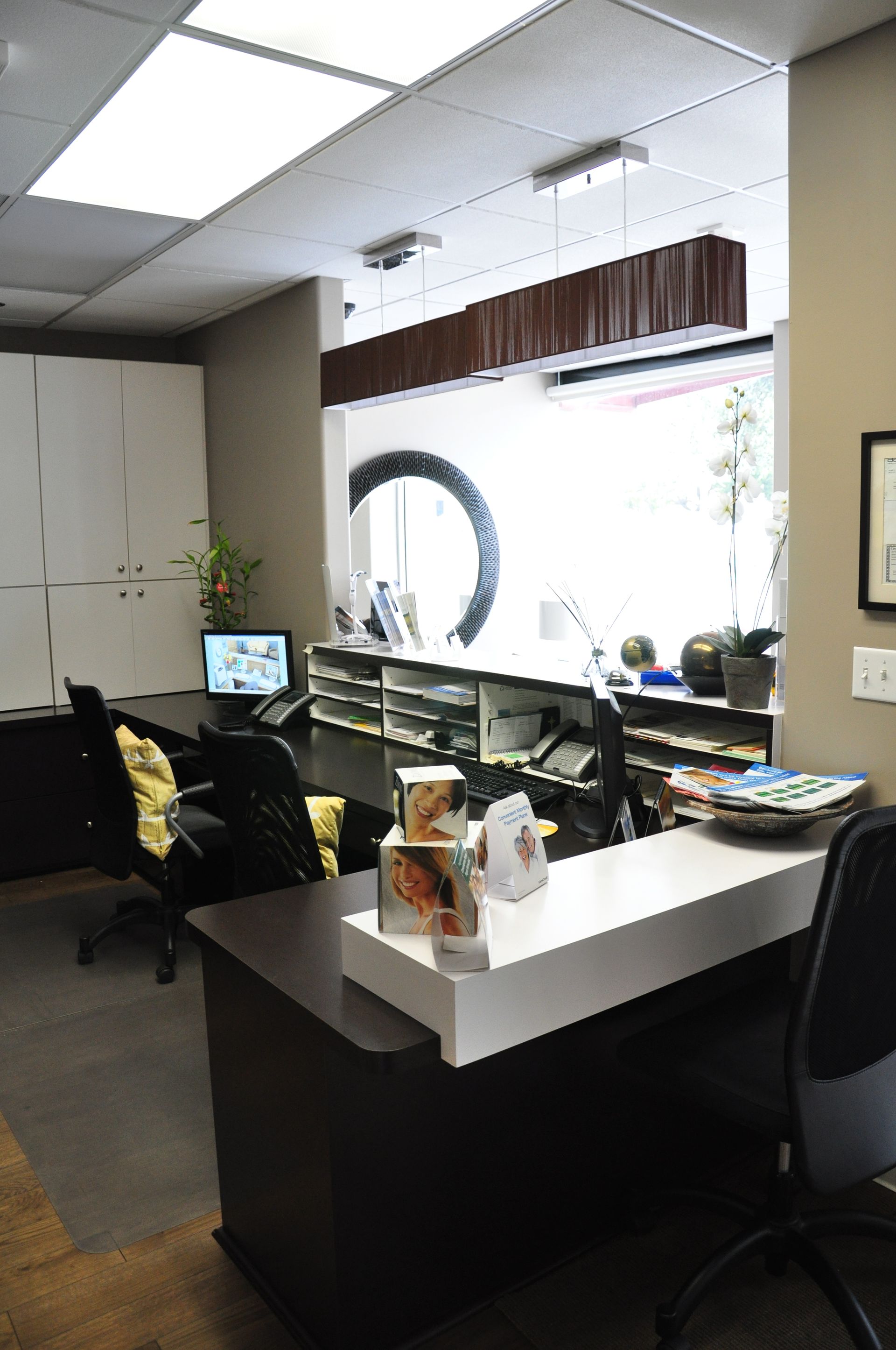 Reception desk in an office with a window view, and a few workstations.