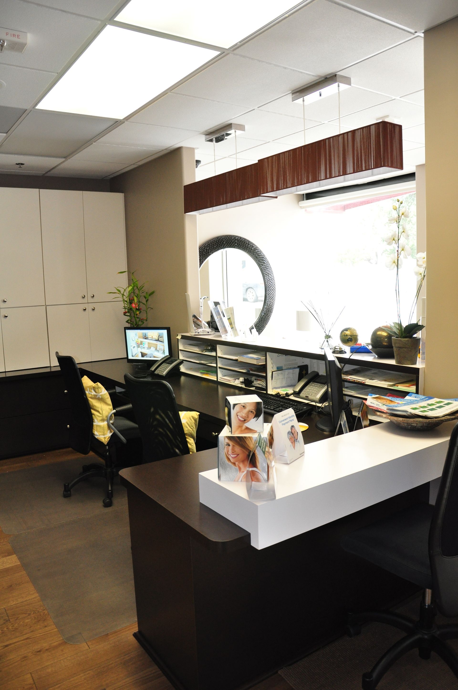 Reception area with dark wood desk, white countertop, window, and black chairs.