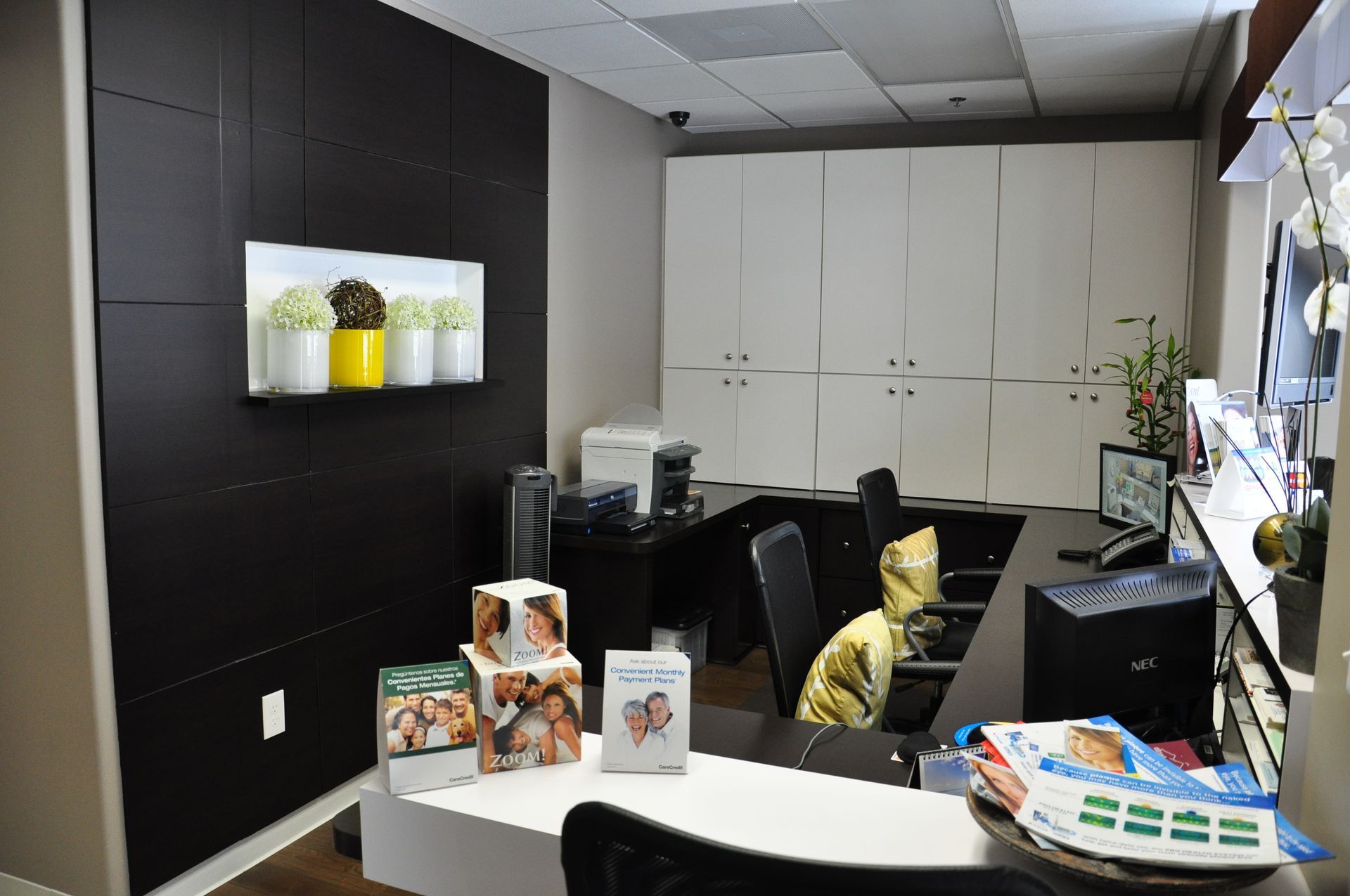 Reception desk with a black accent wall, white cabinets, and flower decorations.