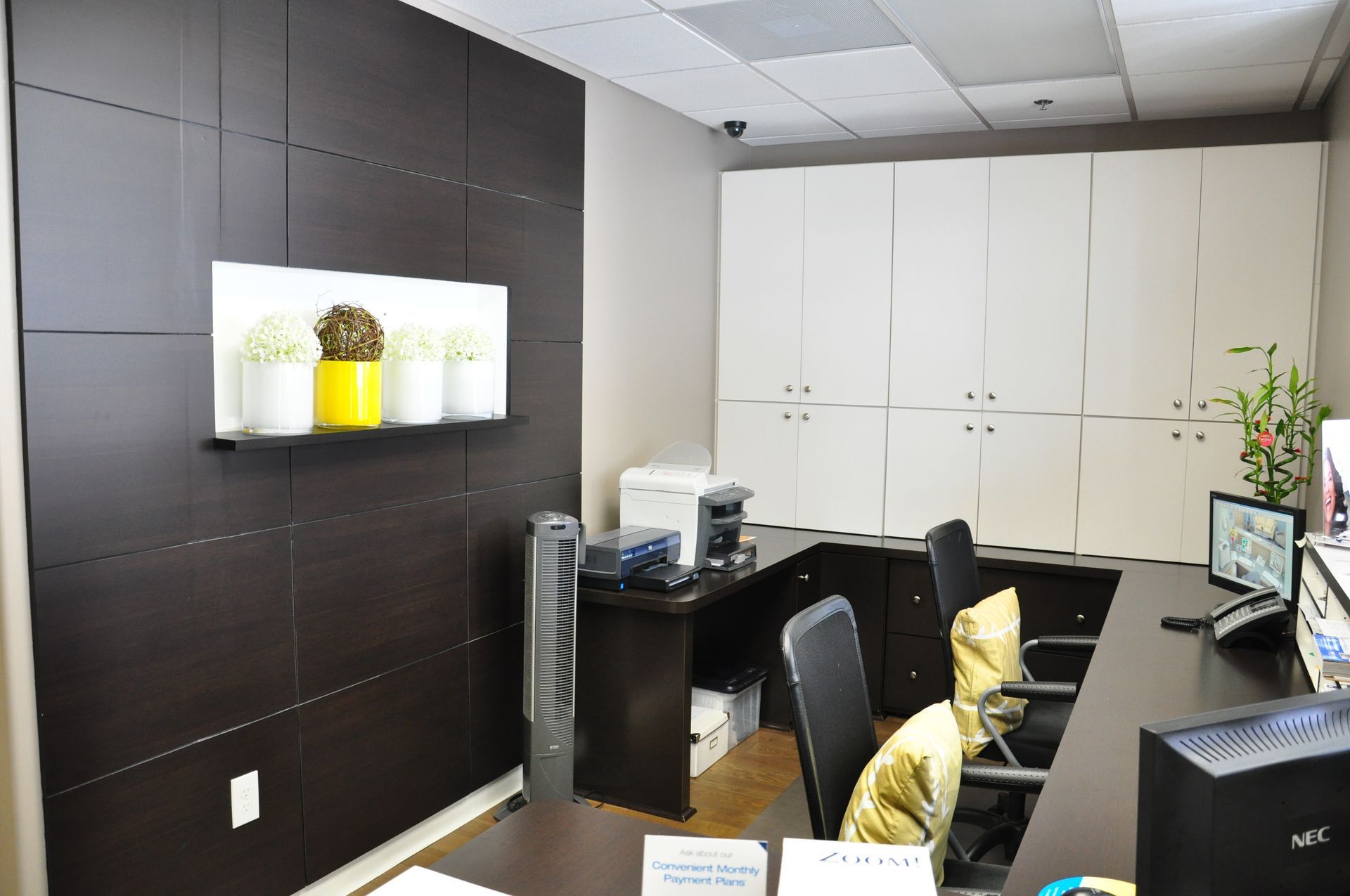 Office with dark accent wall, white cabinets, desk with chairs, and decorative plants.