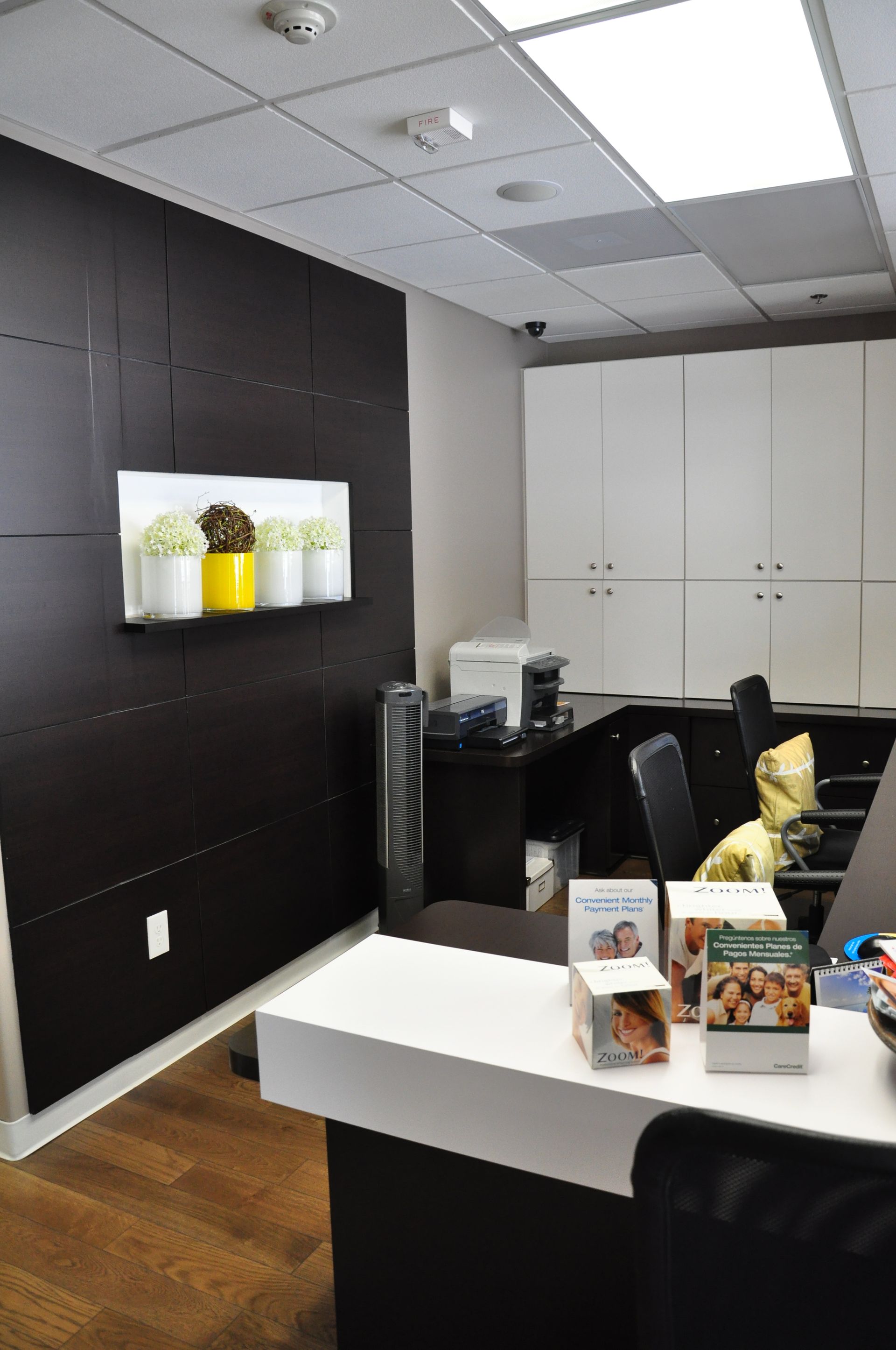 Reception area with white counter, dark wood paneling, art of yellow and white flowers, and white cabinets.