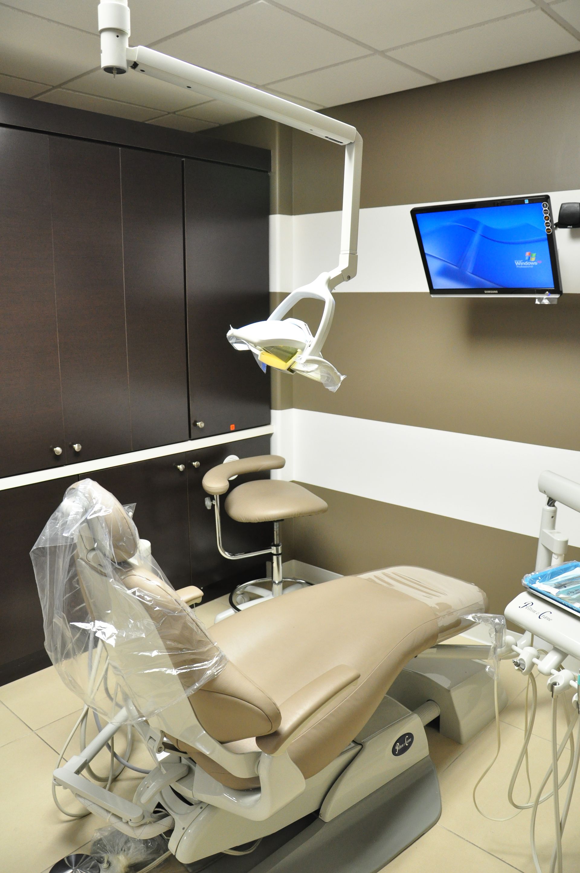 Dentist's chair in a dental office, with a bright overhead light and a wall-mounted computer screen.