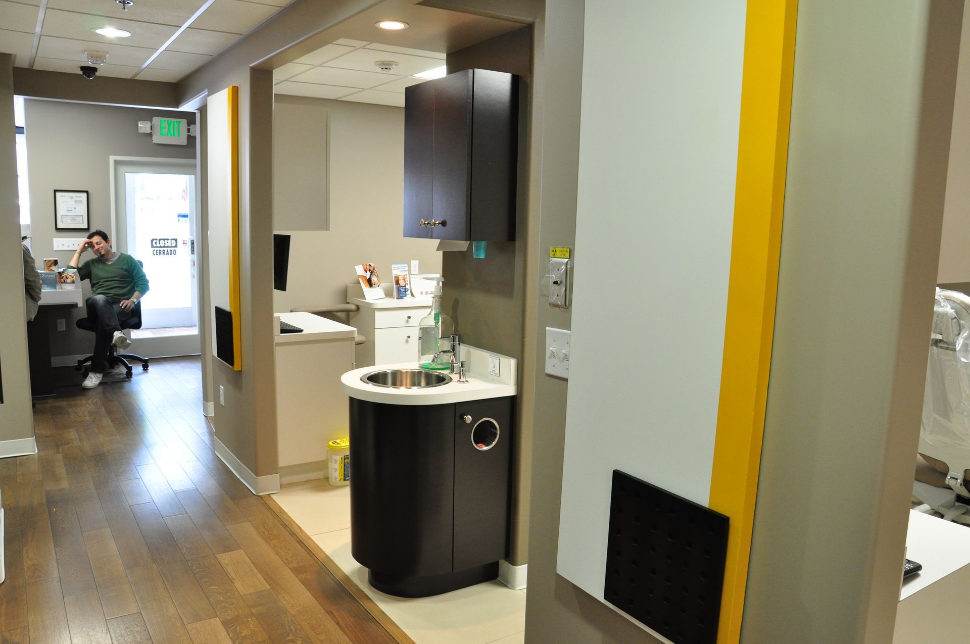 Dental office interior: hallway with sinks, cabinets, and a person at a computer.