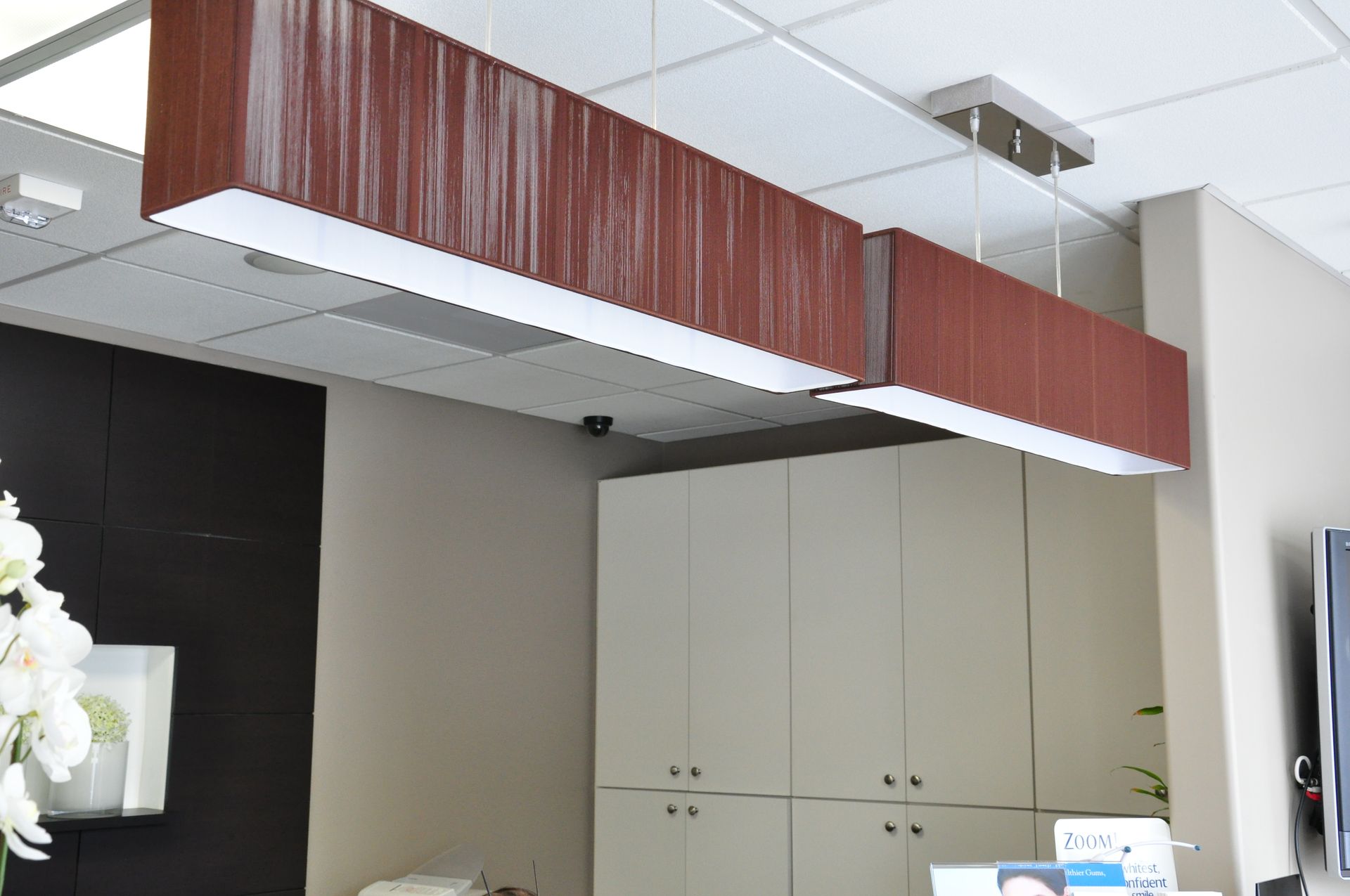 Reception area with brown rectangular light fixtures over a beige counter and cabinets.