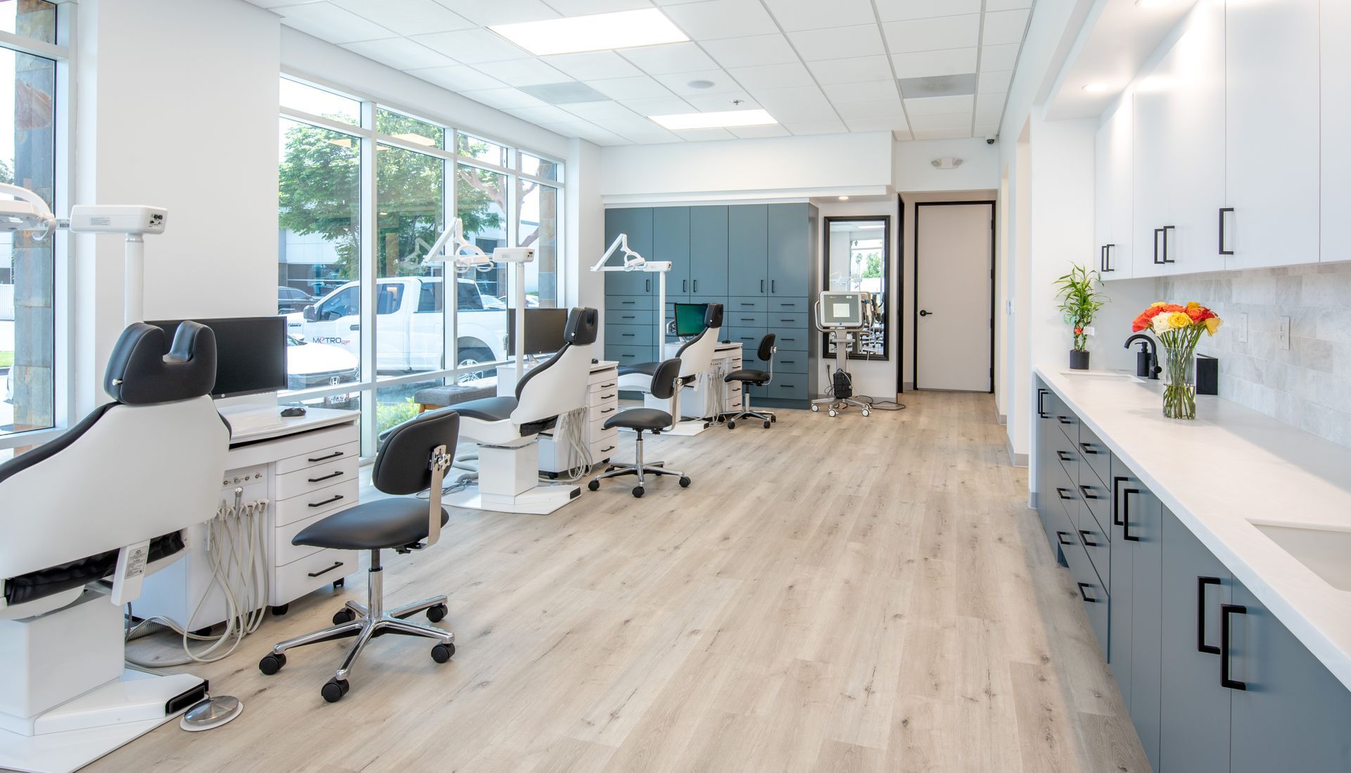 Bright dental office with multiple patient chairs, cabinets, and large windows.