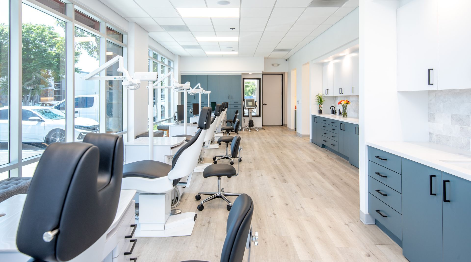 Modern dental office interior with chairs, equipment, windows, and cabinets.