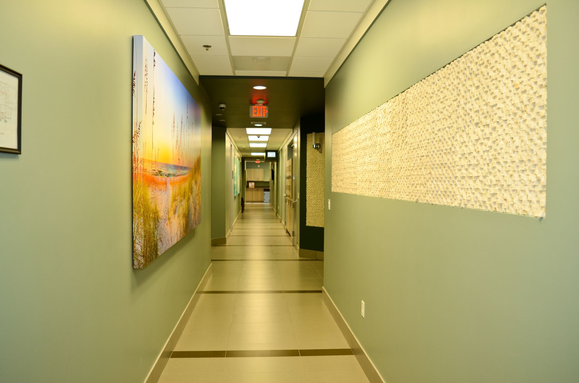 Long hallway with green walls, artwork, and a textured wall panel.