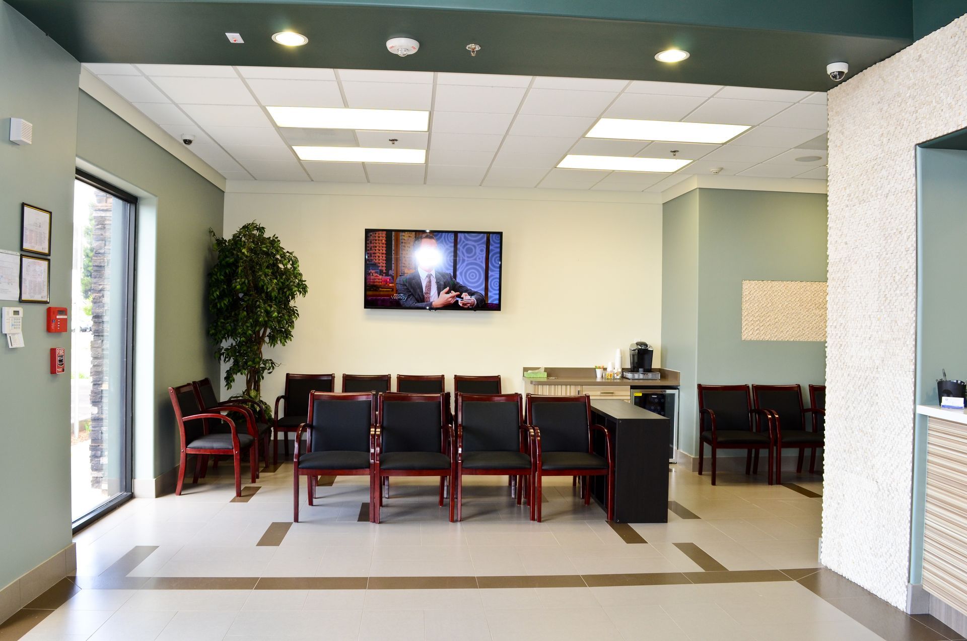 A medical waiting room with chairs, TV, a coffee machine, and an entryway.