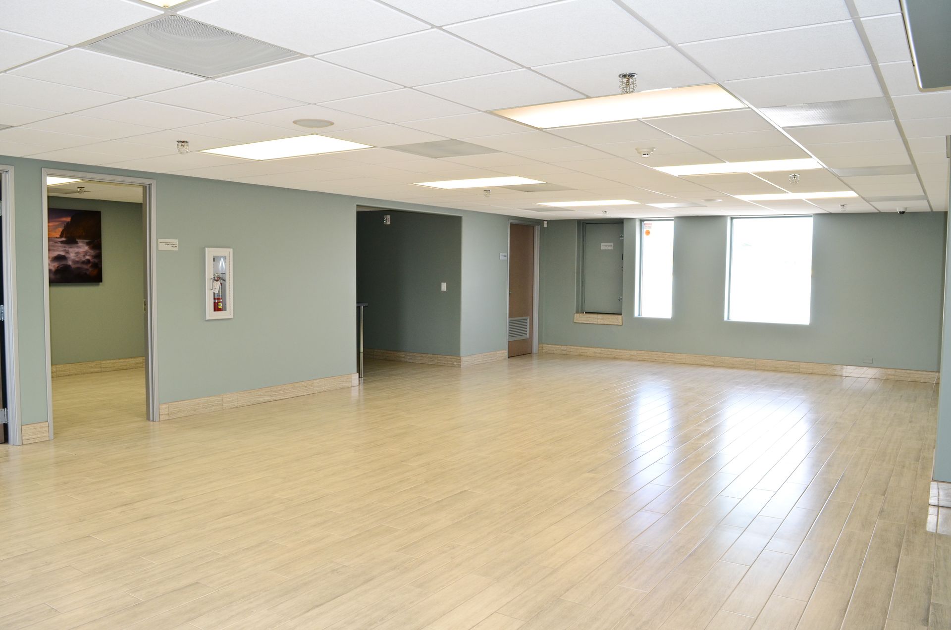 Empty room with light wood floors, pale green walls, and ceiling lights. Includes doorways and windows.