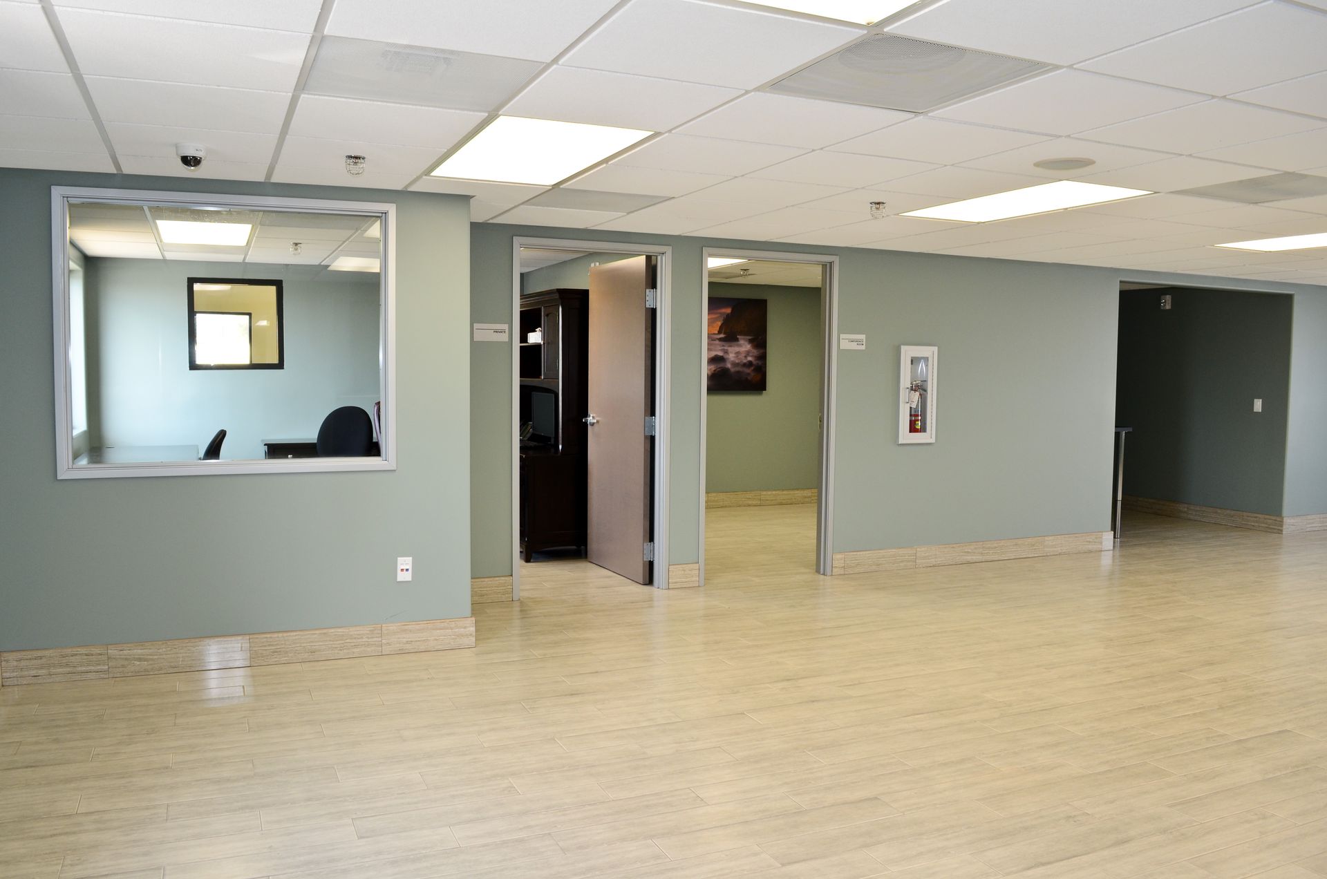 Empty office interior with pale green walls, beige floor, and three open doorways.