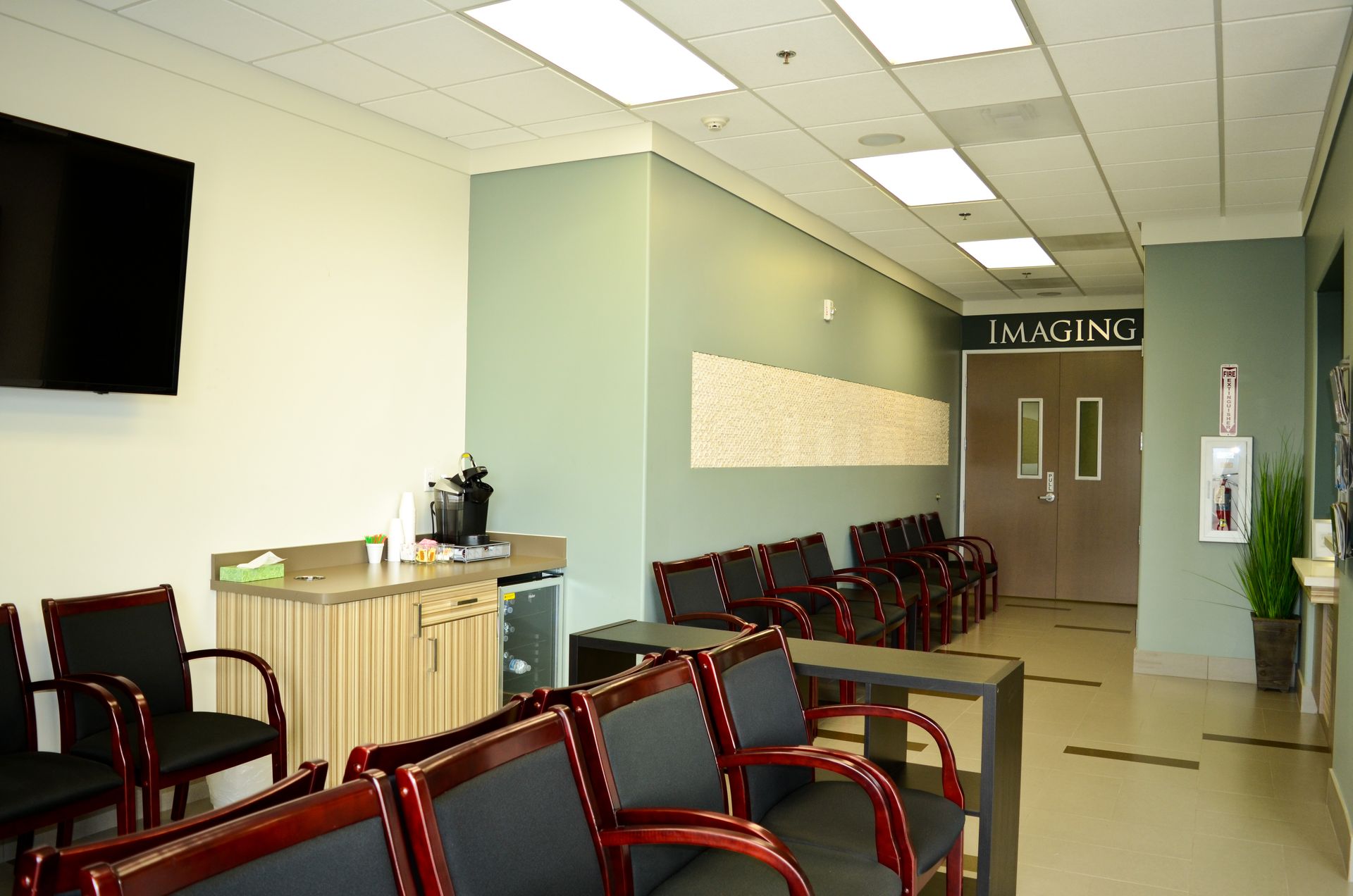 A waiting room with black chairs, a coffee station, and a door labeled 