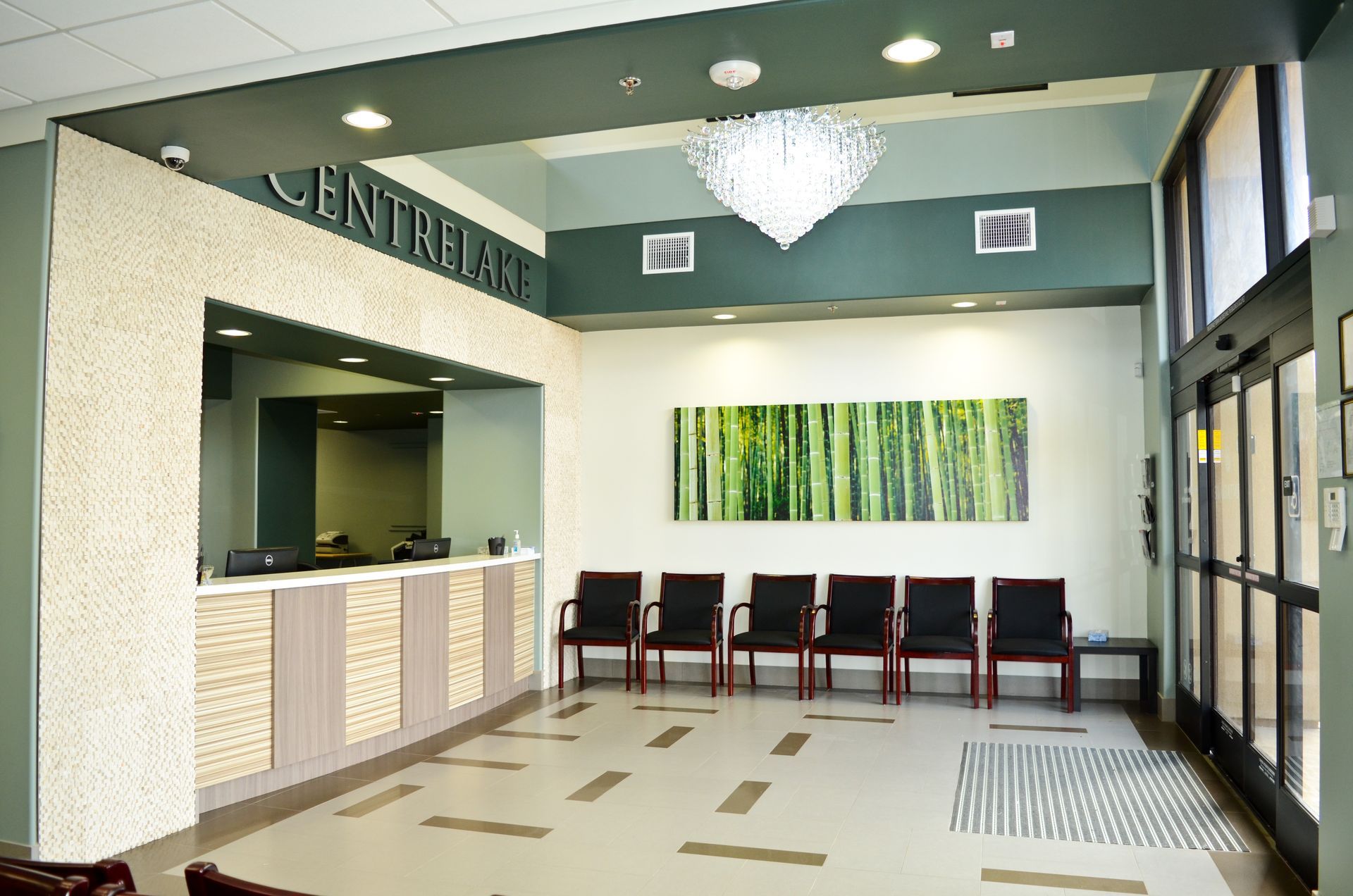 Reception area with a check-in counter, chairs, and a bamboo-themed art piece; overhead chandelier.