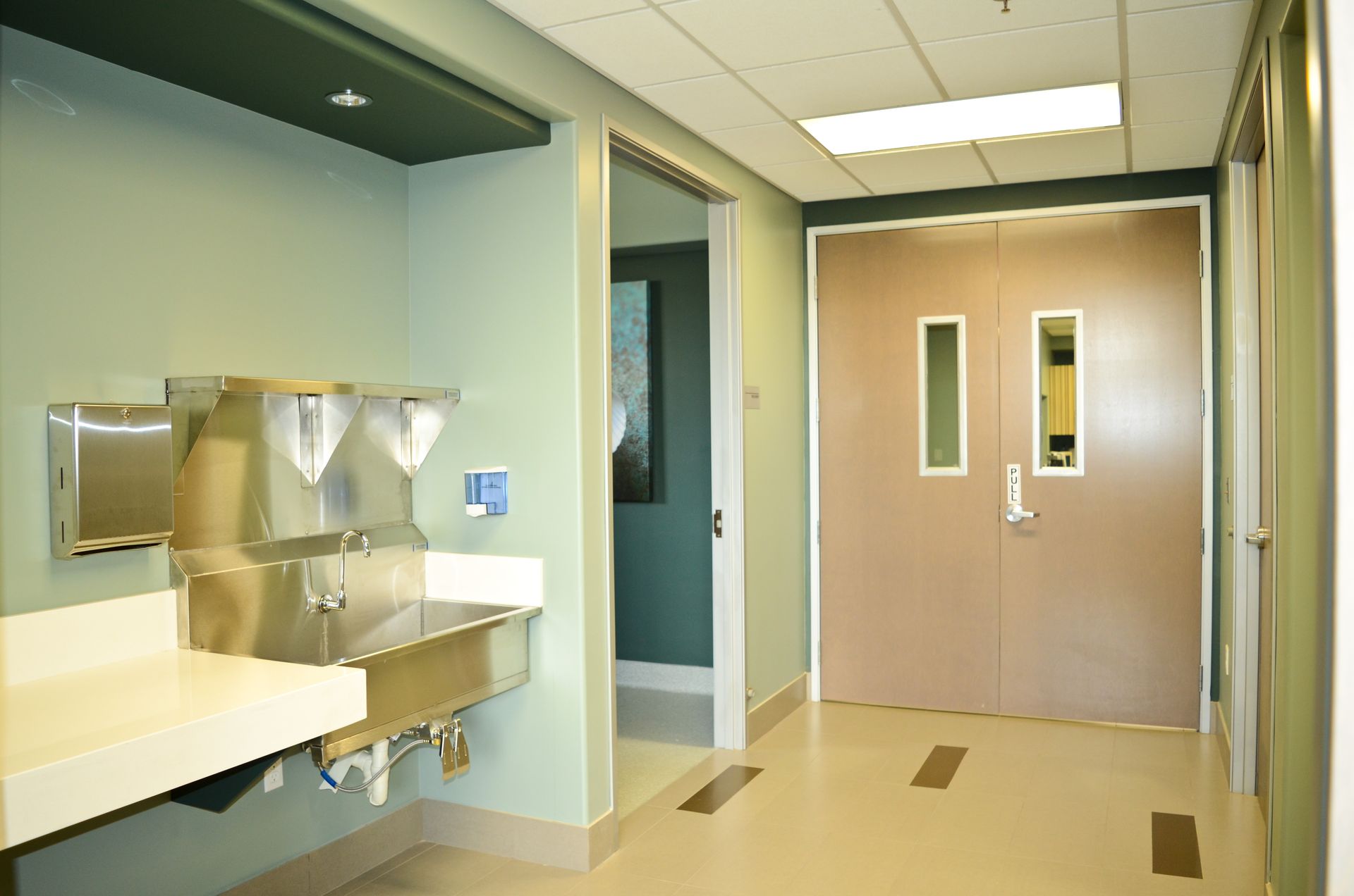 Hospital hallway with sink, doorway, and double doors, light tan and green color scheme.