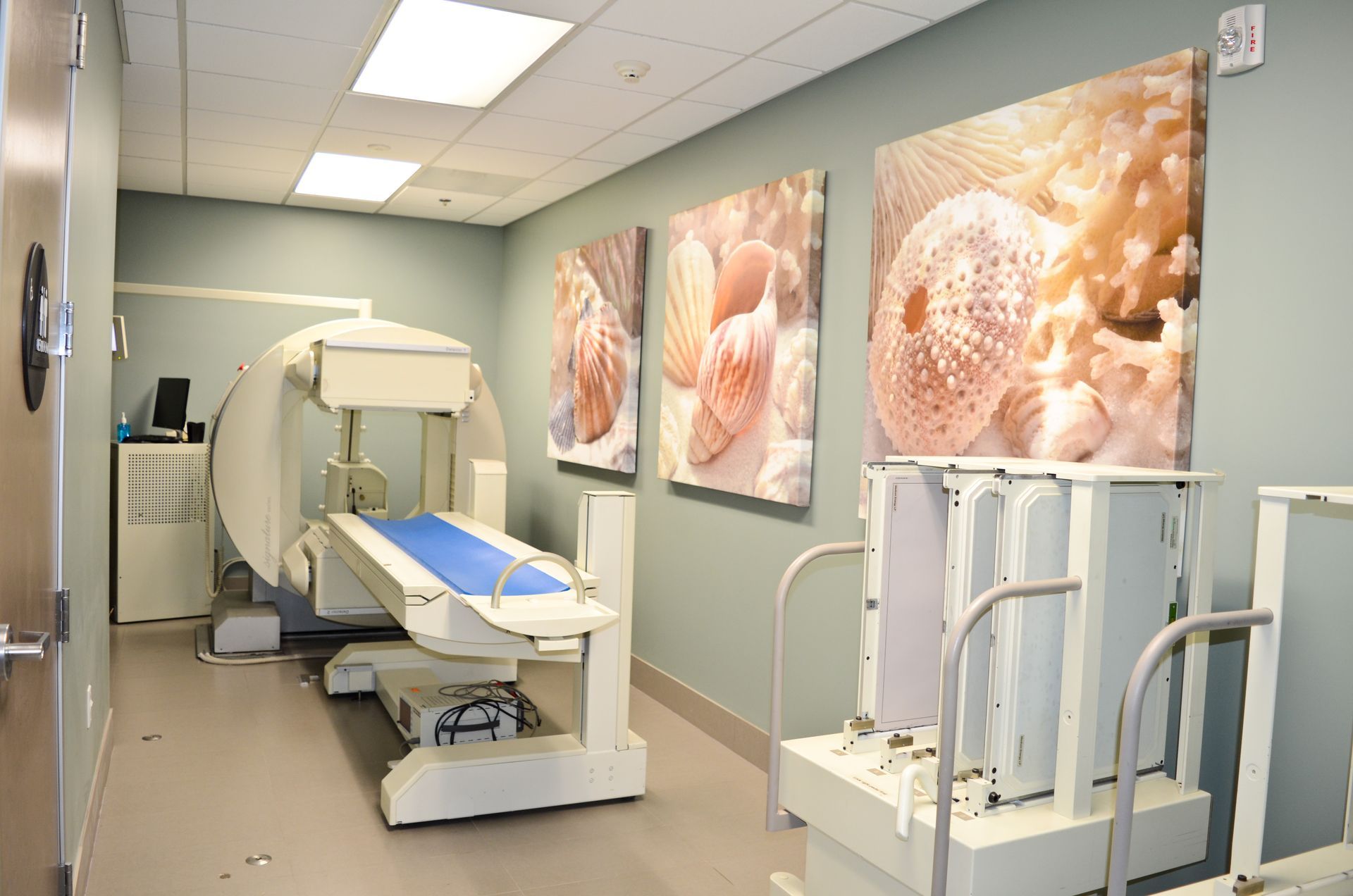 A medical room with a large machine and an examination table, decorative wall art, and medical equipment.