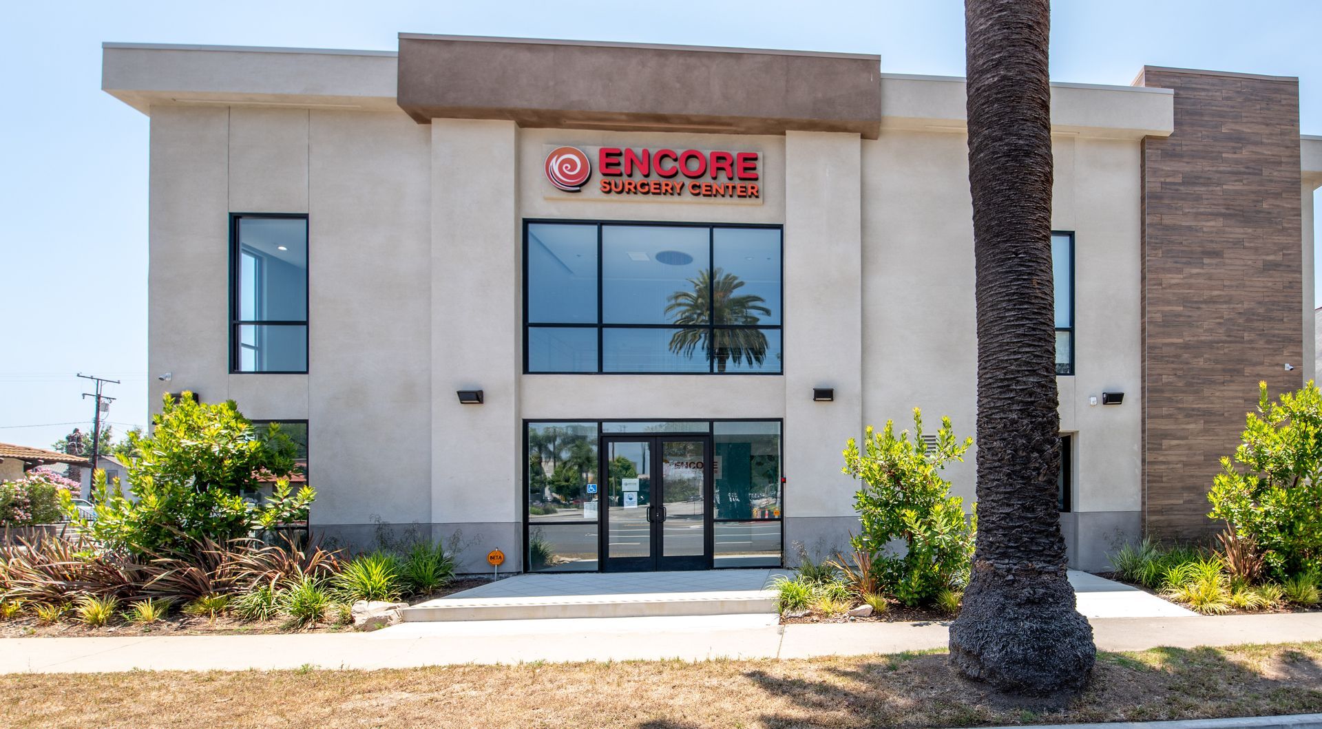 Encore Personal Injury office exterior, beige building with red logo, palm tree in front.