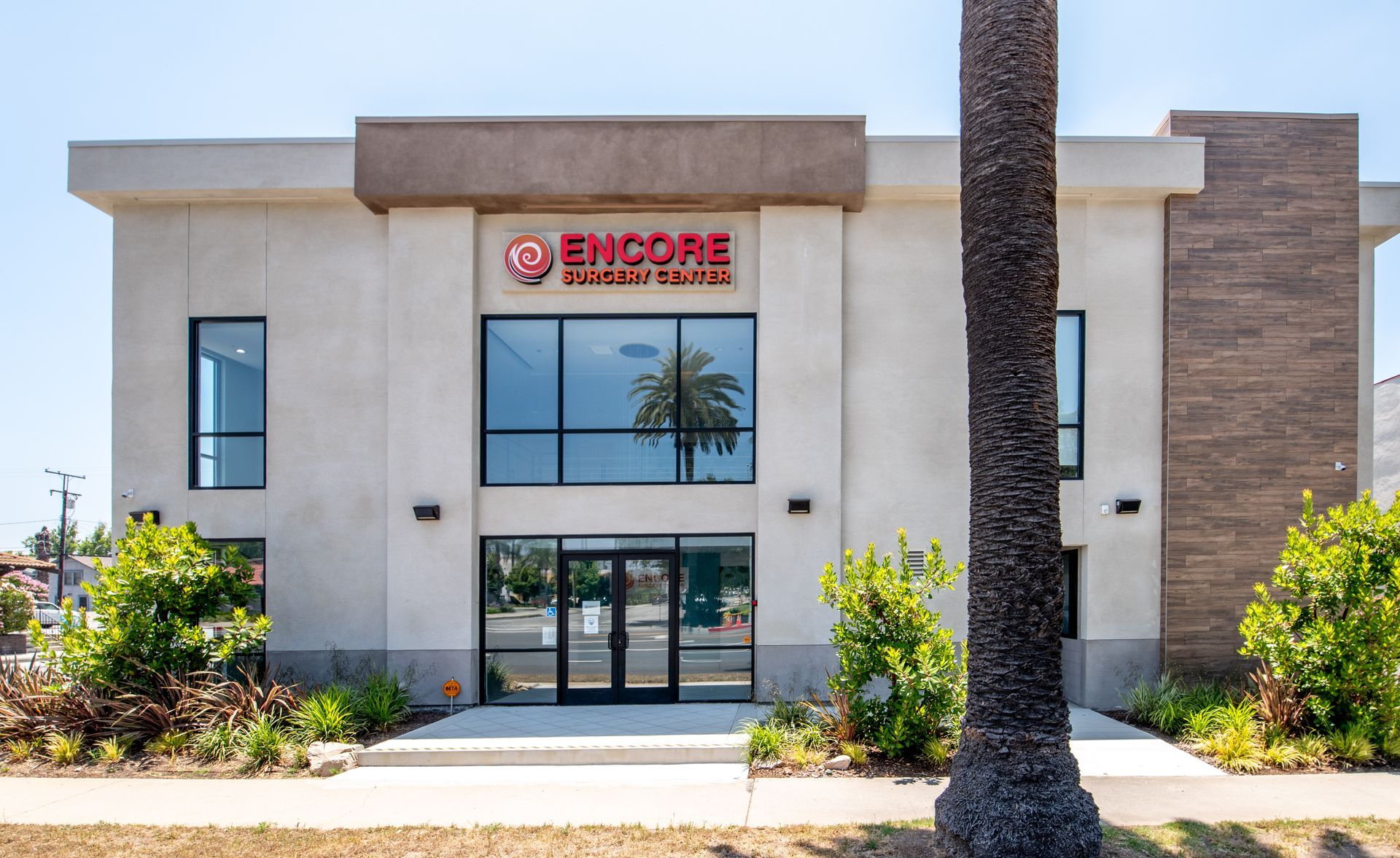 Encore Urgent Center building with red logo, glass doors, windows, and a palm tree outside.