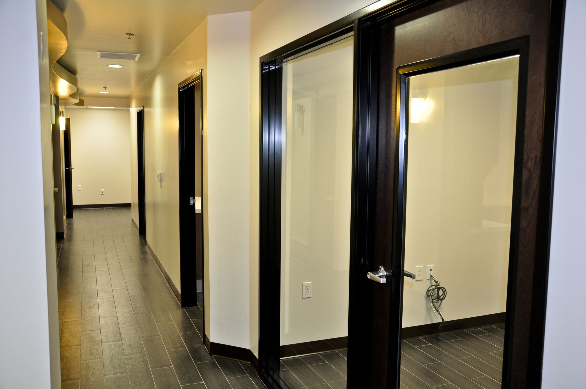 Office hallway with dark wood doors and flooring, white walls.