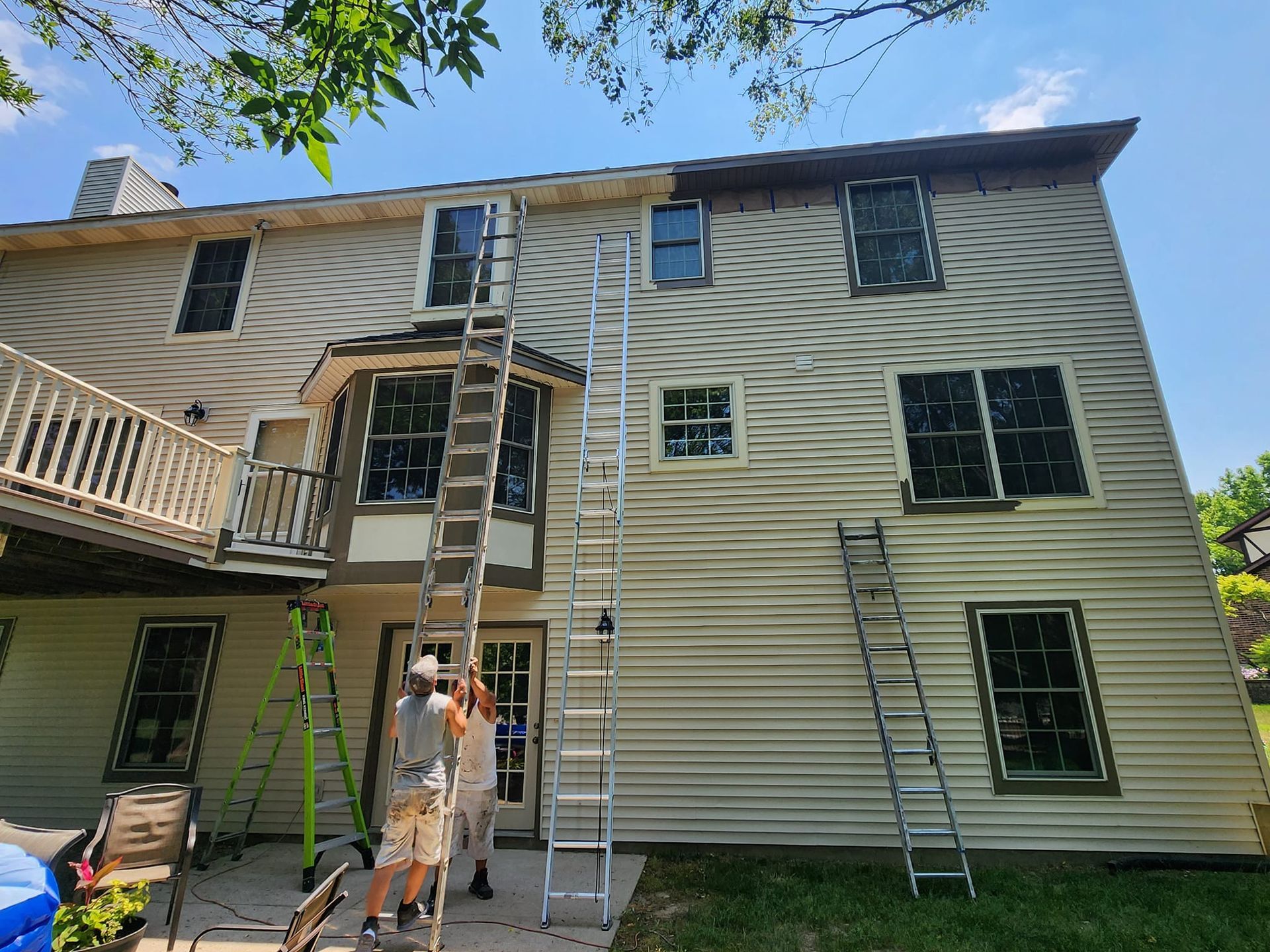 A man is standing on a ladder in front of a large house.