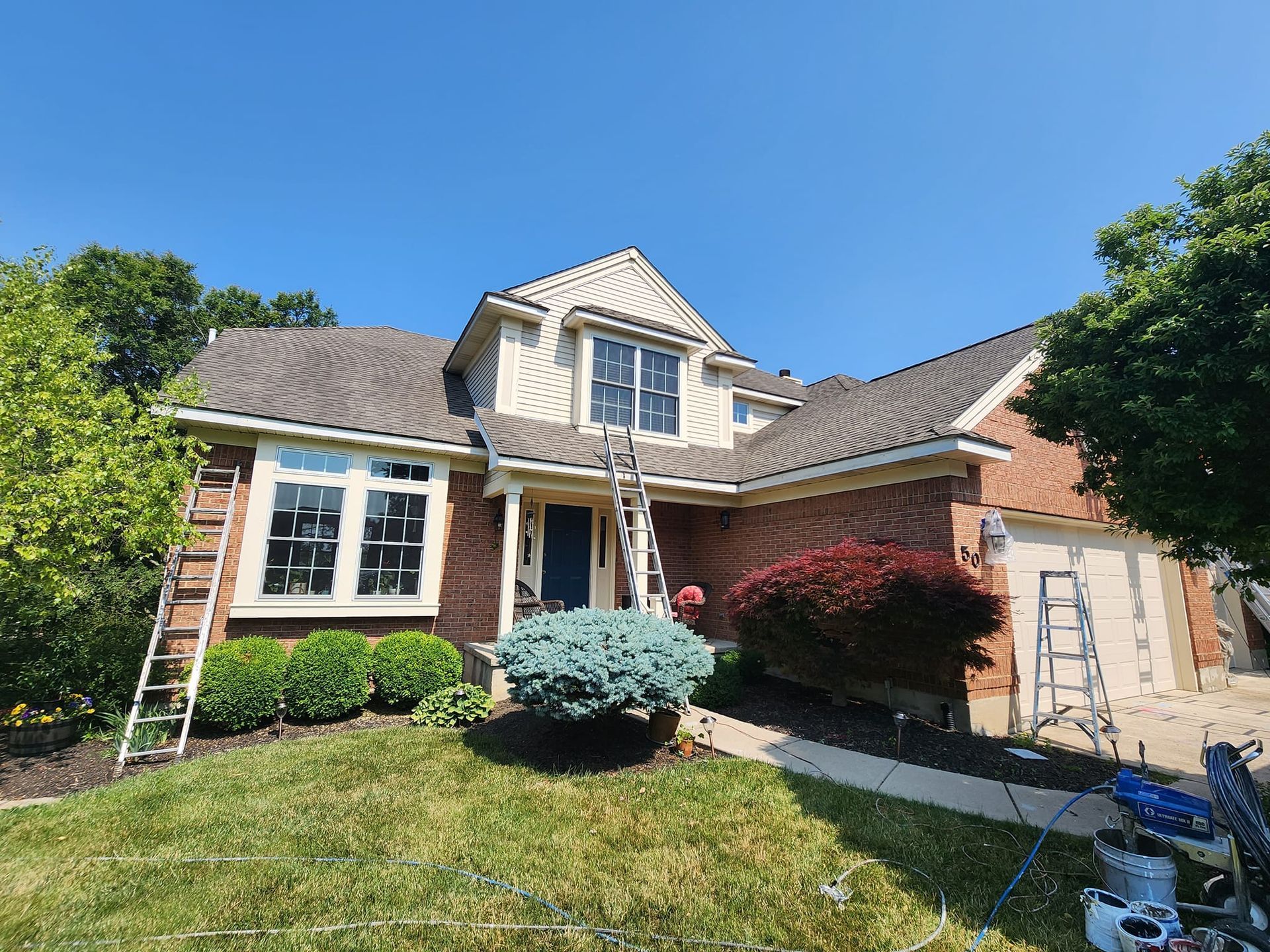 A brick house is being painted with a ladder in front of it.
