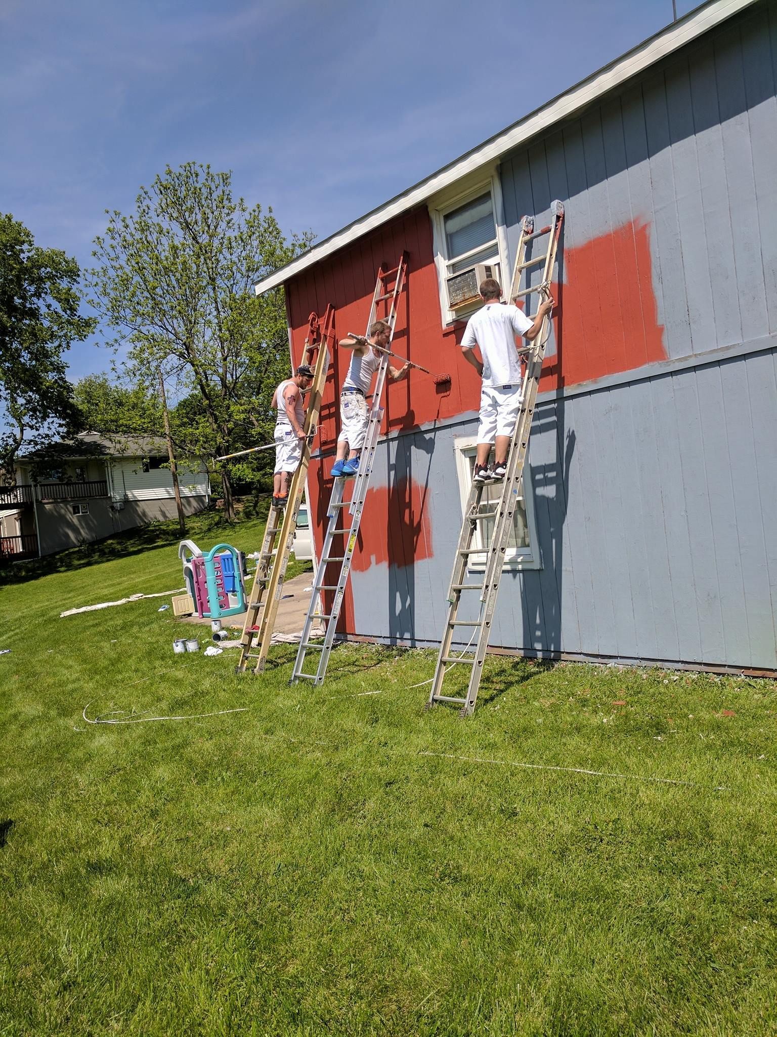 A group of people are painting a house with ladders.