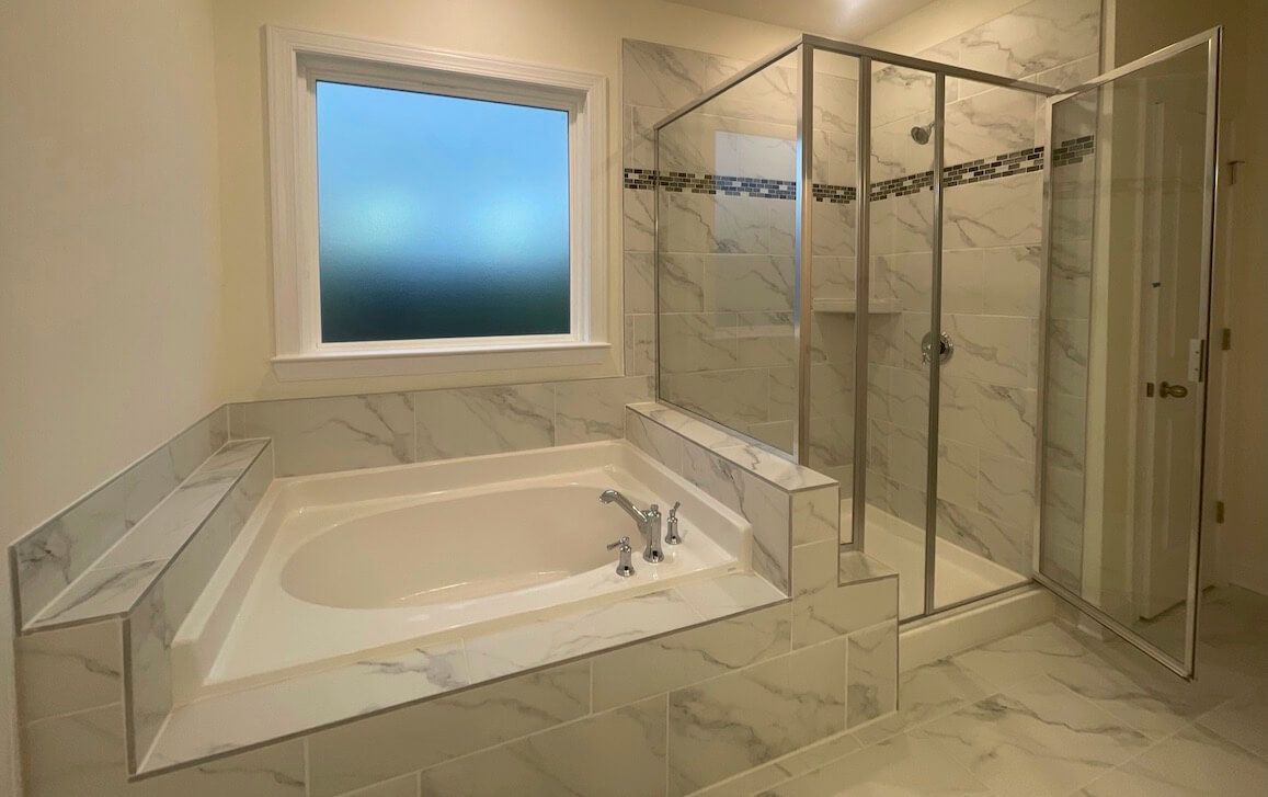 Bathroom with a soaking tub and glass shower; marble tile, window with sky view.
