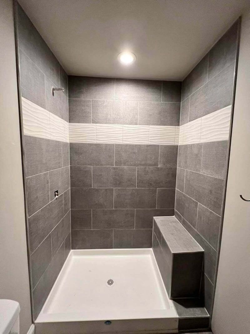 Gray tiled walk-in shower with a built-in bench, white base, and accent stripe.