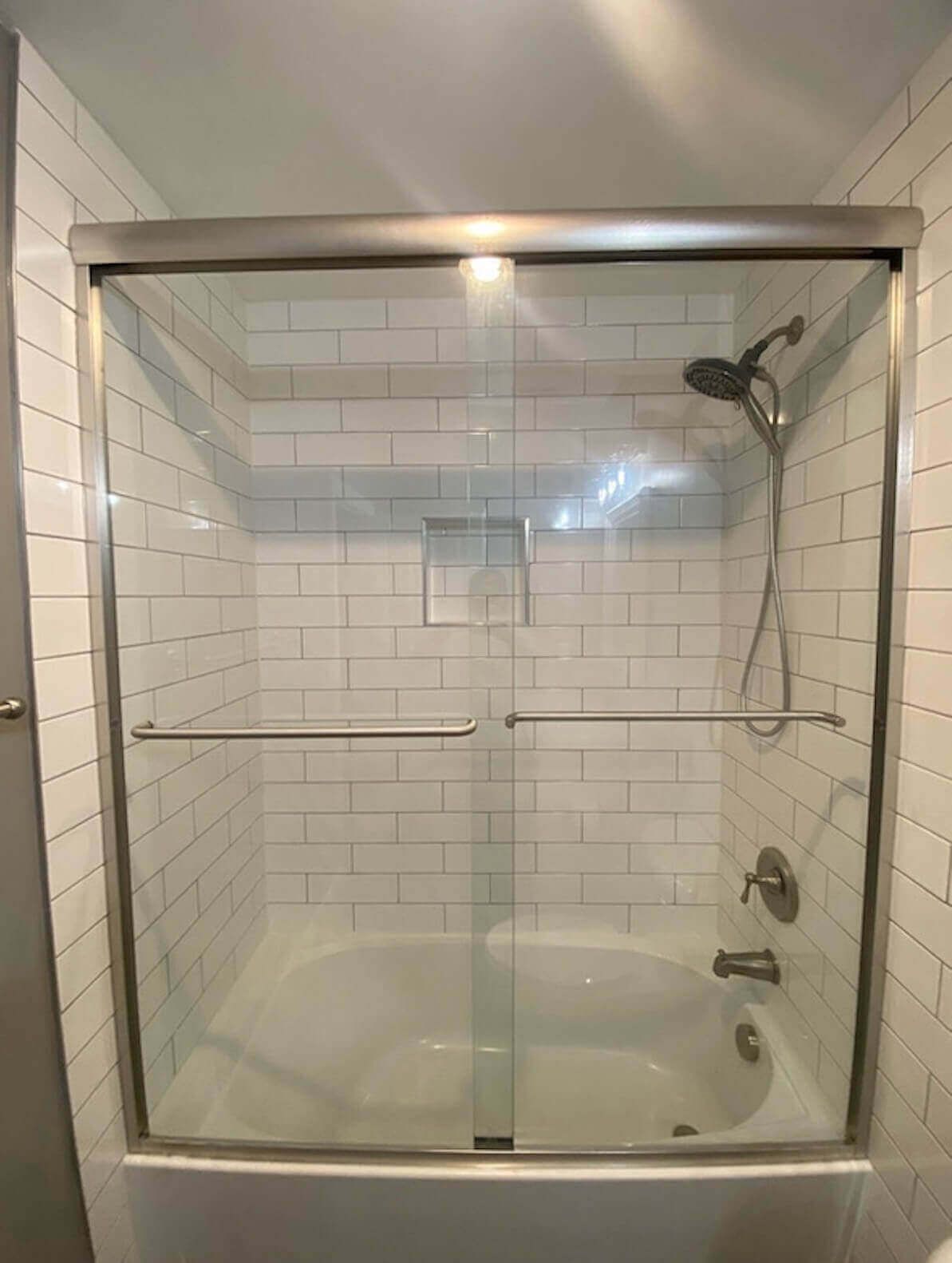 A white tiled shower with a glass sliding door, a shower head, and a bathtub inside.
