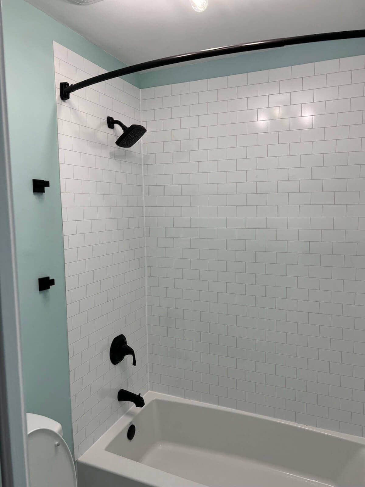 A small bathroom with white tiled shower and black fixtures; the wall is a light blue.