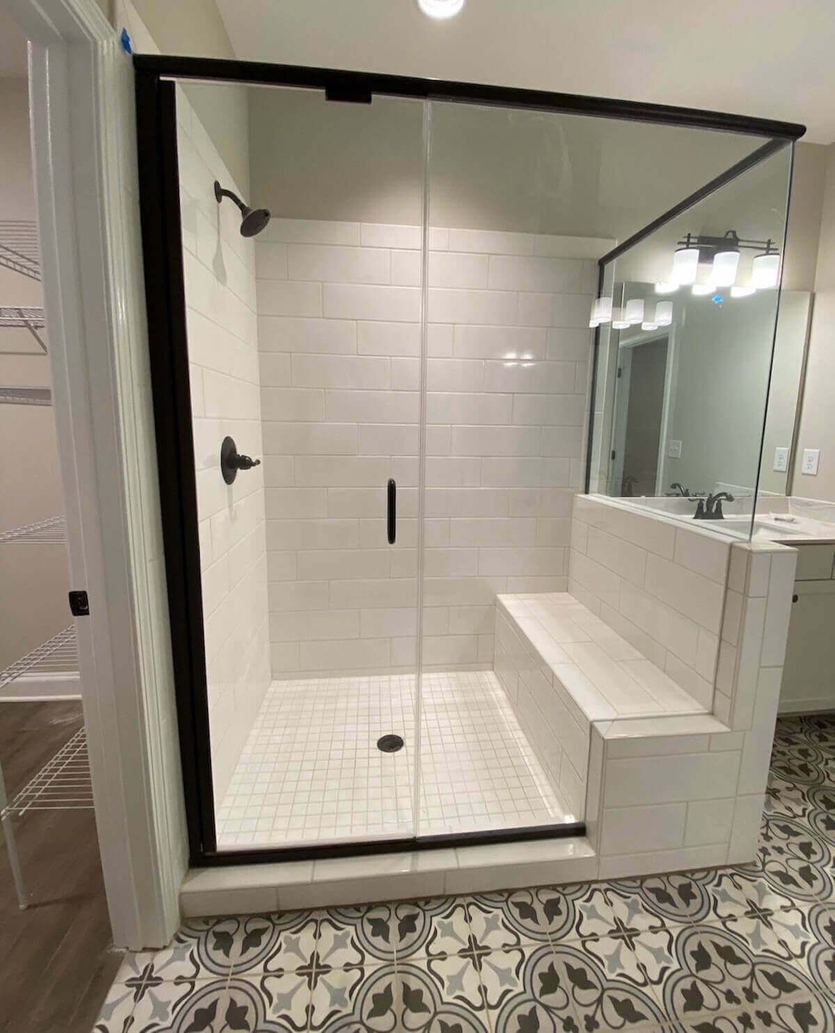 Modern shower stall with black frame, white subway tile, bench, and patterned floor.