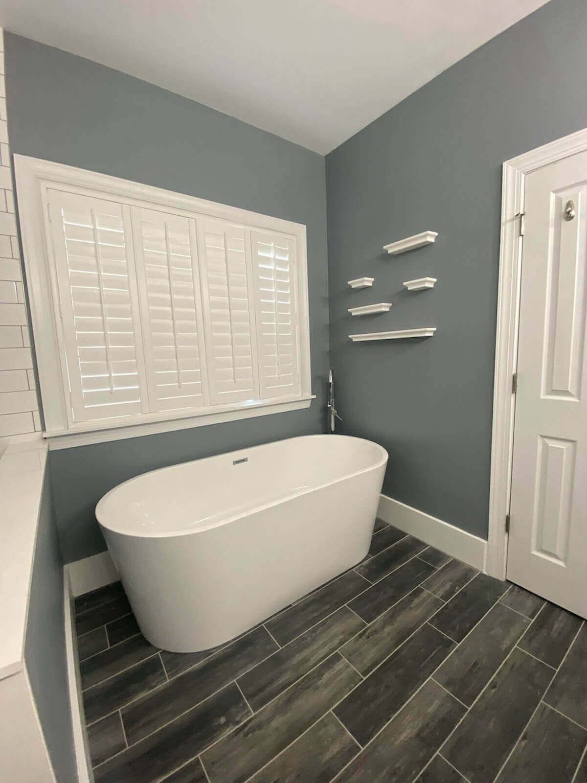 Modern bathroom with white oval tub, gray walls, and wood-look tile floor.