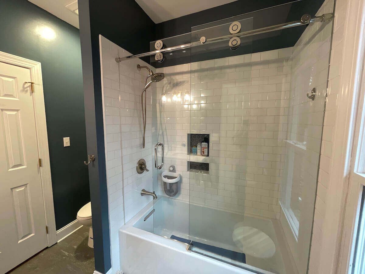 Bathroom with white tile shower, sliding glass door, and dark blue wall.
